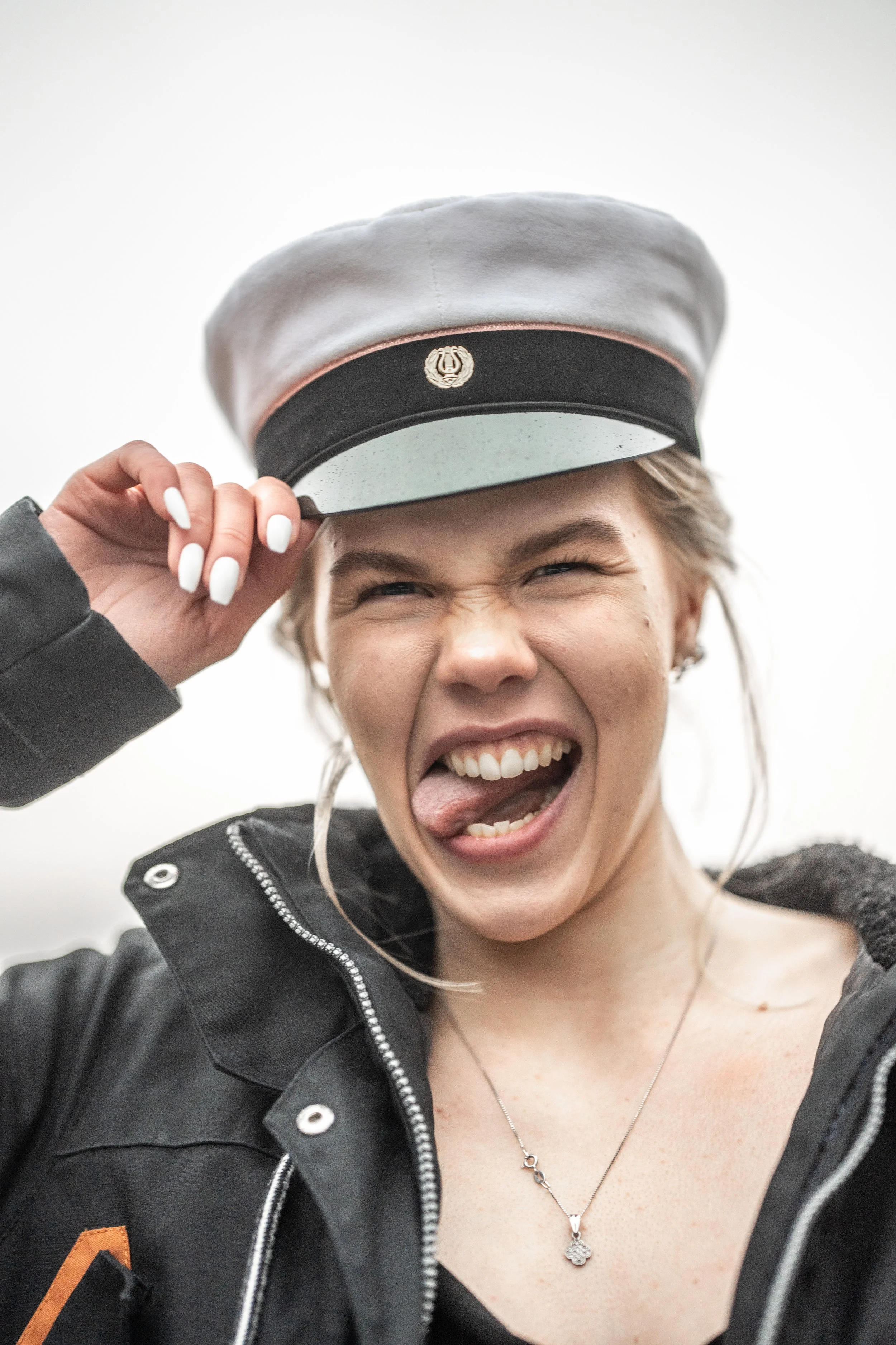 Young woman wearing a cap, sticking out her tongue, and making a playful expression.