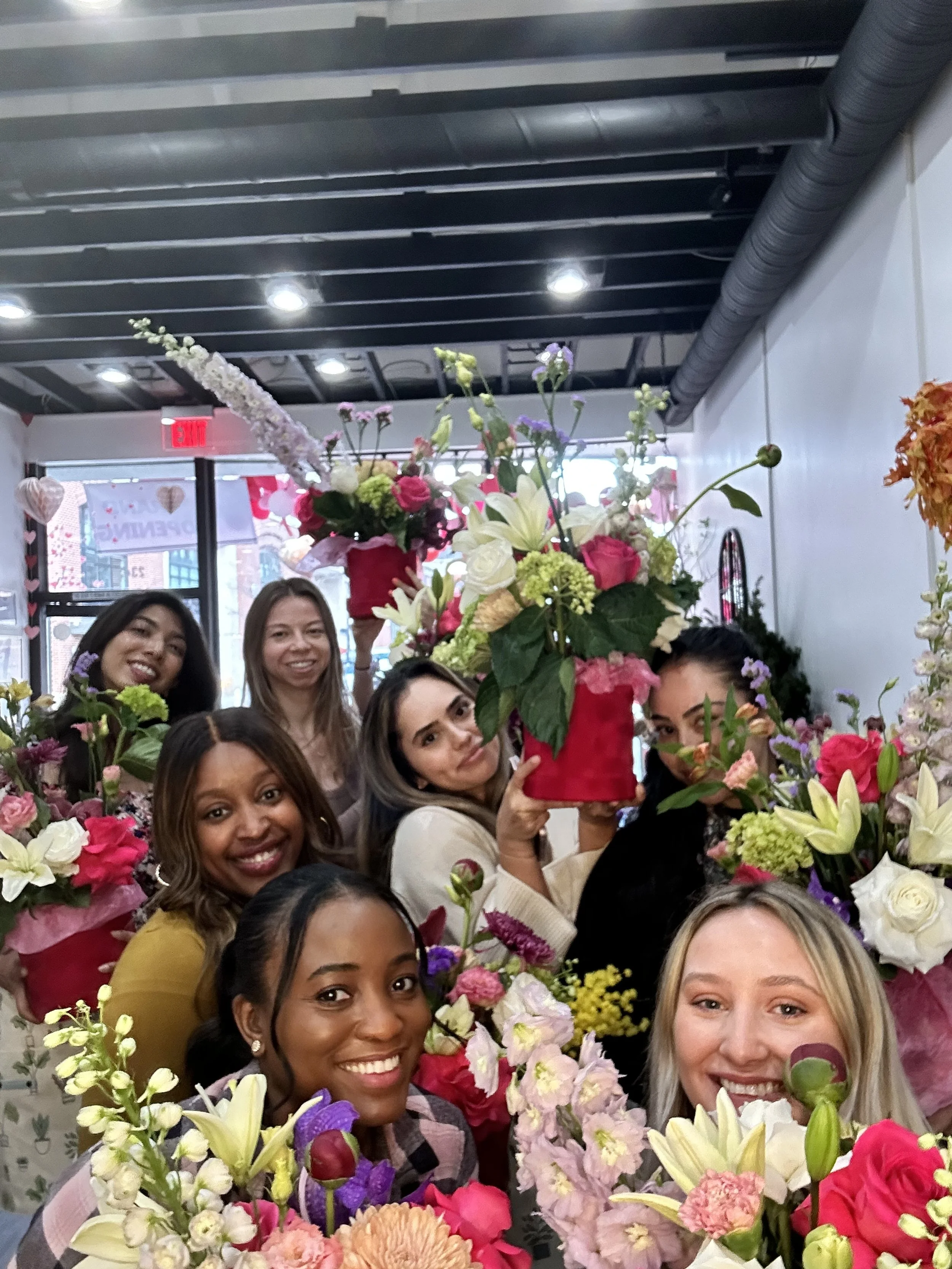 Group of women holding colorful flower arrangements inside a flower shop.