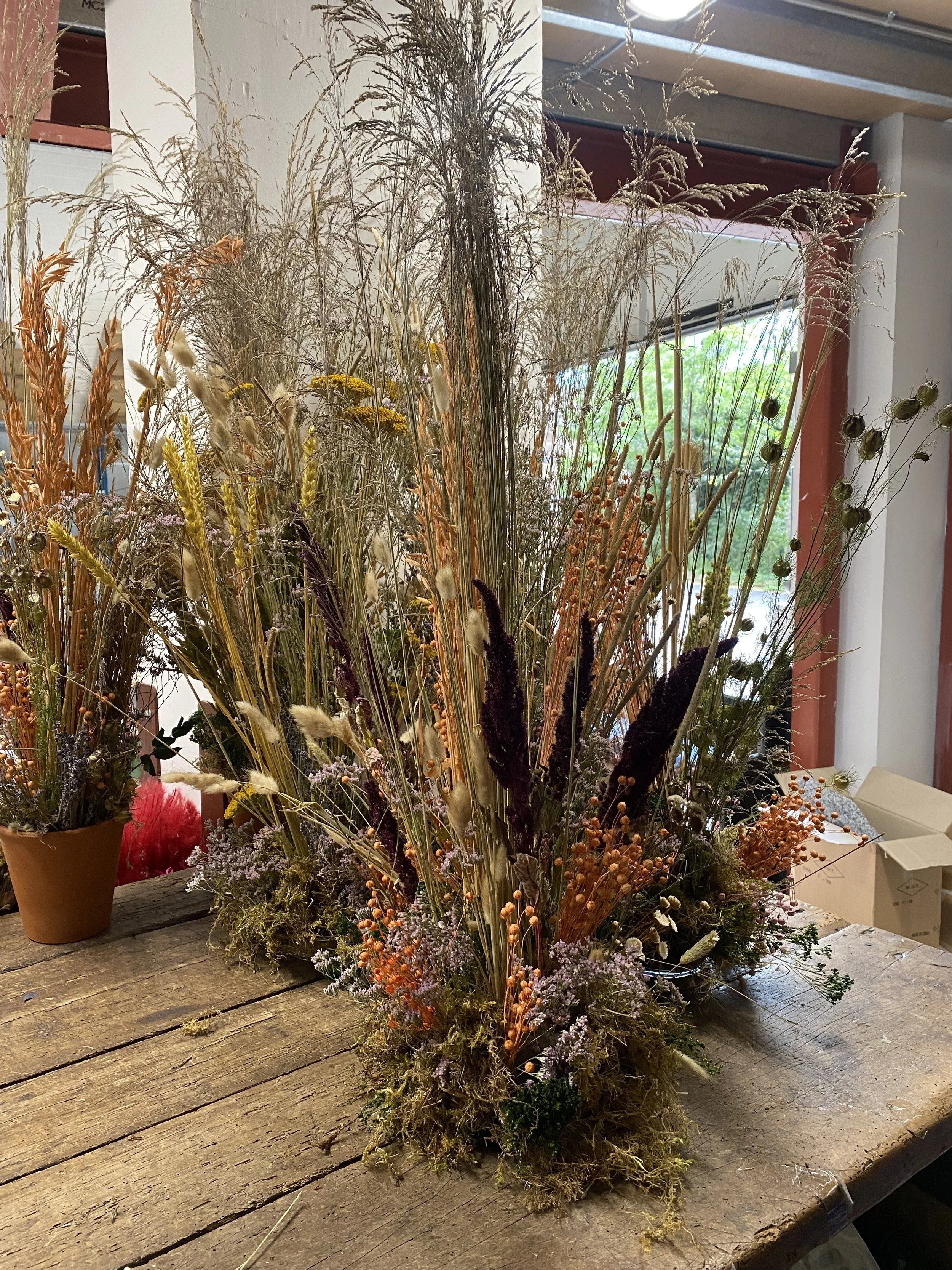A large bouquet of dried wildflowers and grasses on a rustic wooden table in a well-lit room.