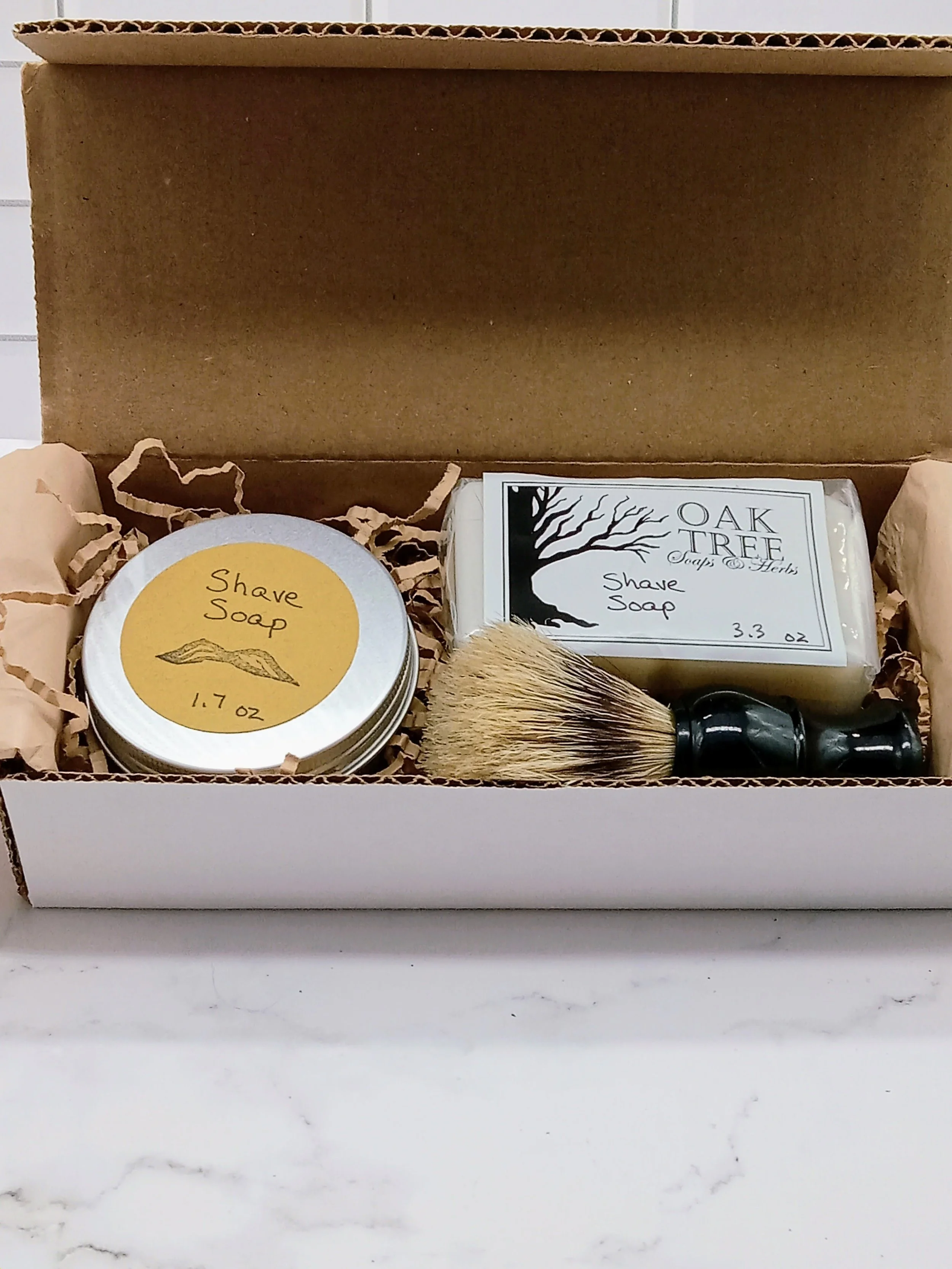 Image shows box with round tin containing shave soap, two pack of square soap refills, and a shave brush.