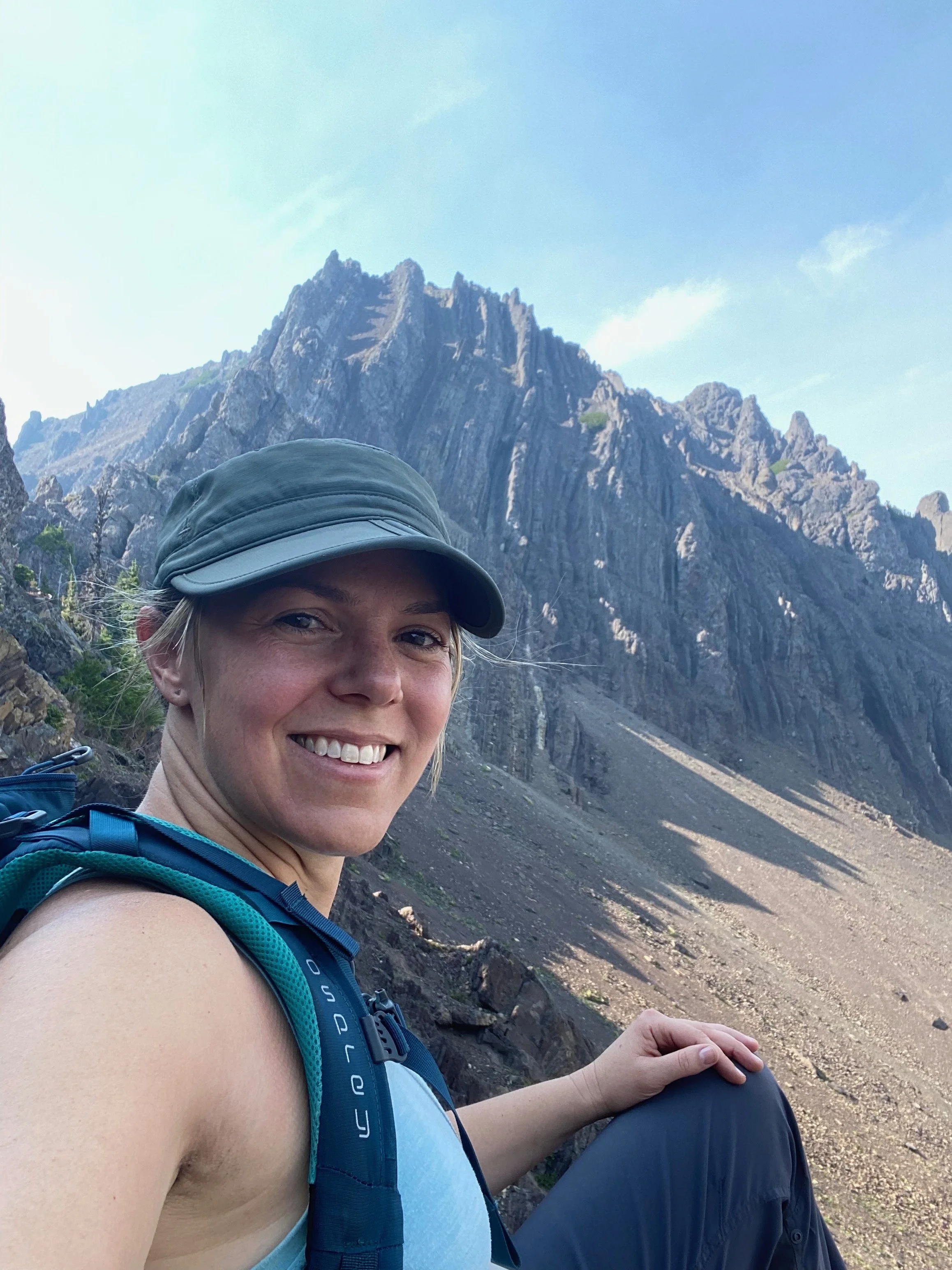 Stephanie sitting on top of a mountain feeling alive, accomplished, and proud of this accomplishment.