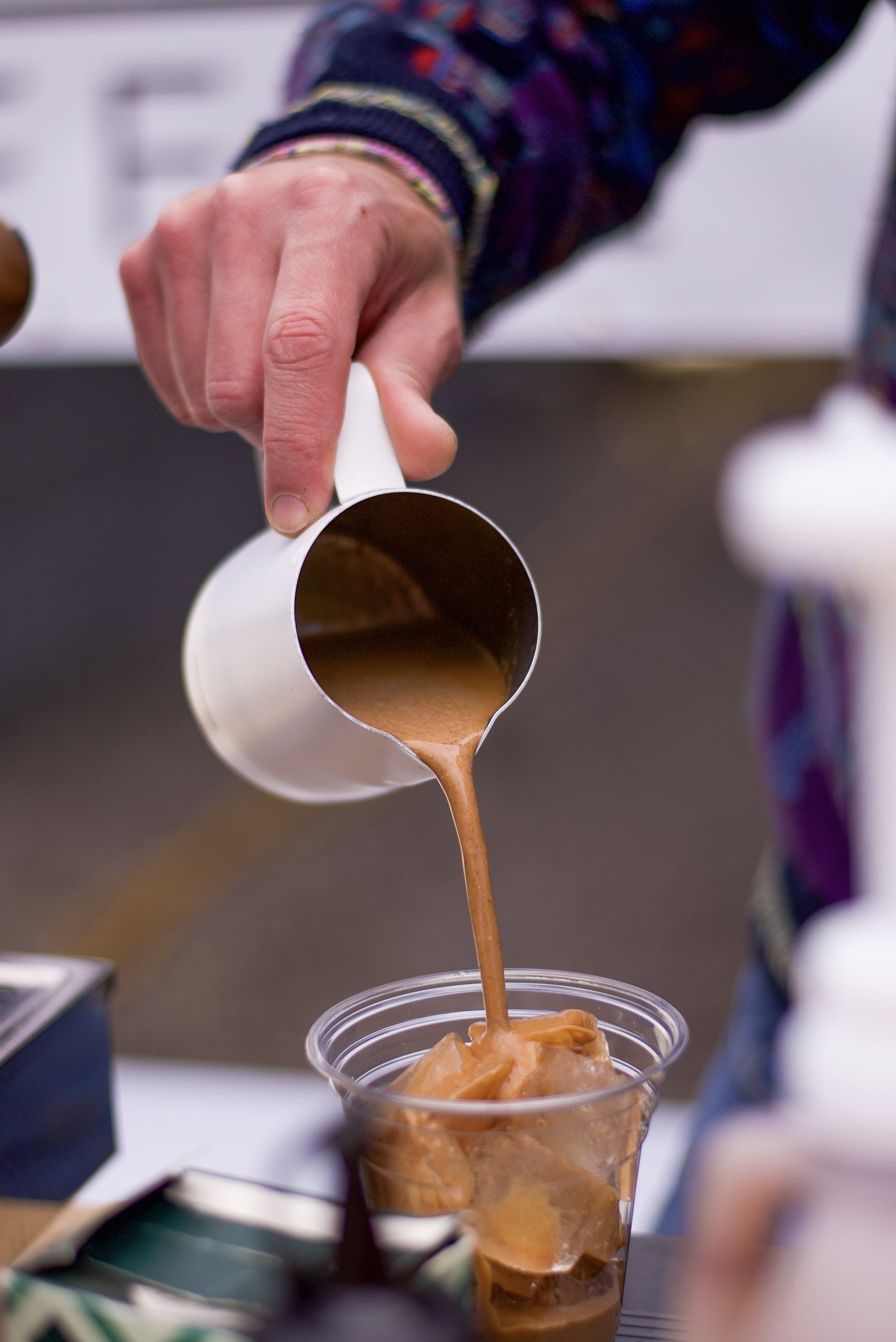 Person pouring coffee into a clear plastic cup with ice.
