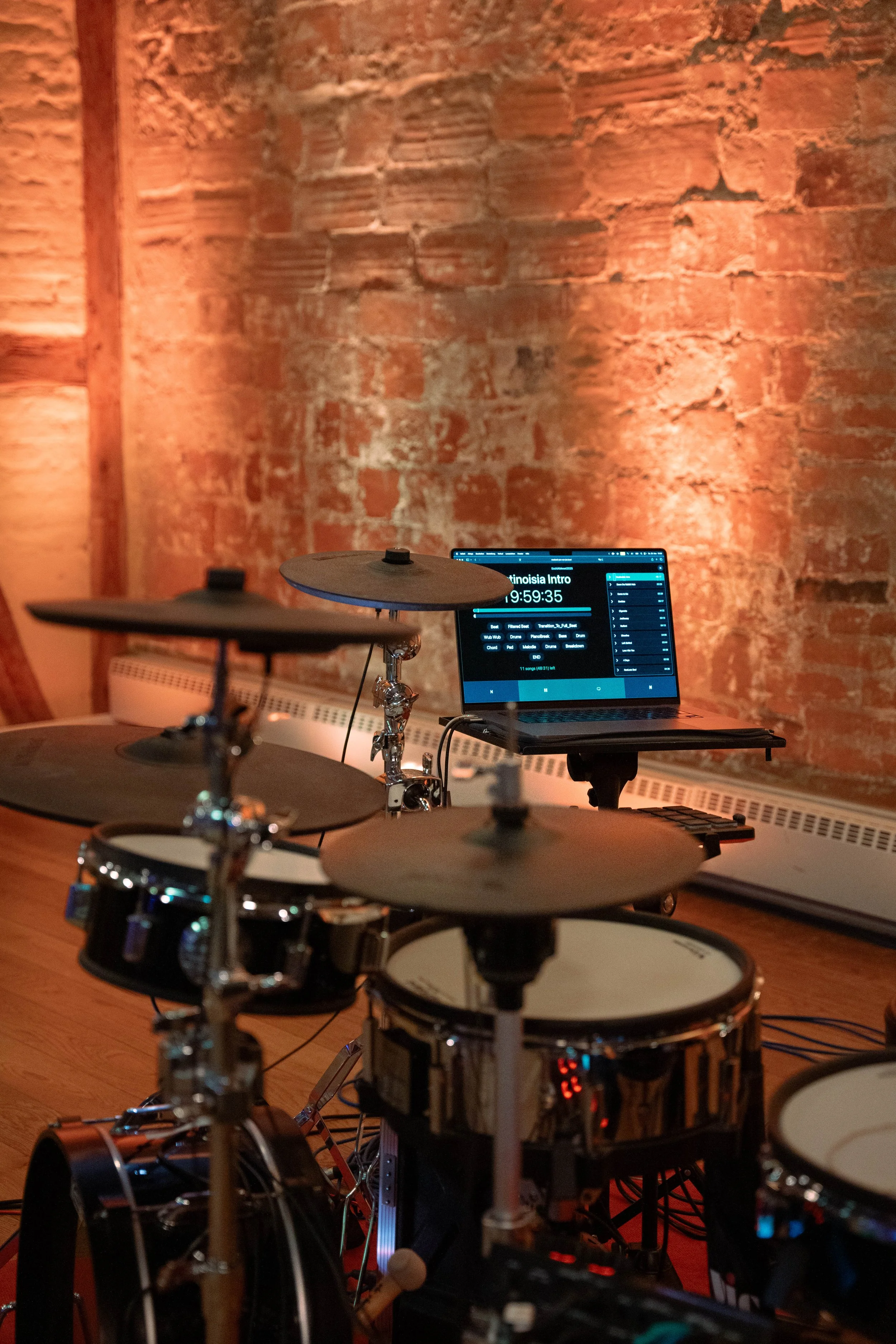 Ein elektronisches Schlagzeug vor einer roten Backsteinmauer mit einem Laptop im Hintergrund.