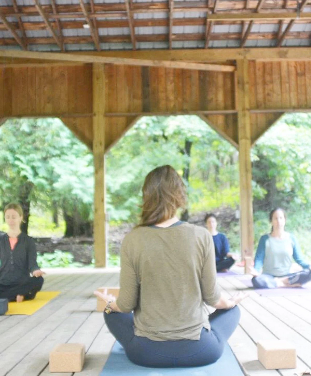 Women practicing yoga outdoors in a wooden pavilion surrounded by trees.