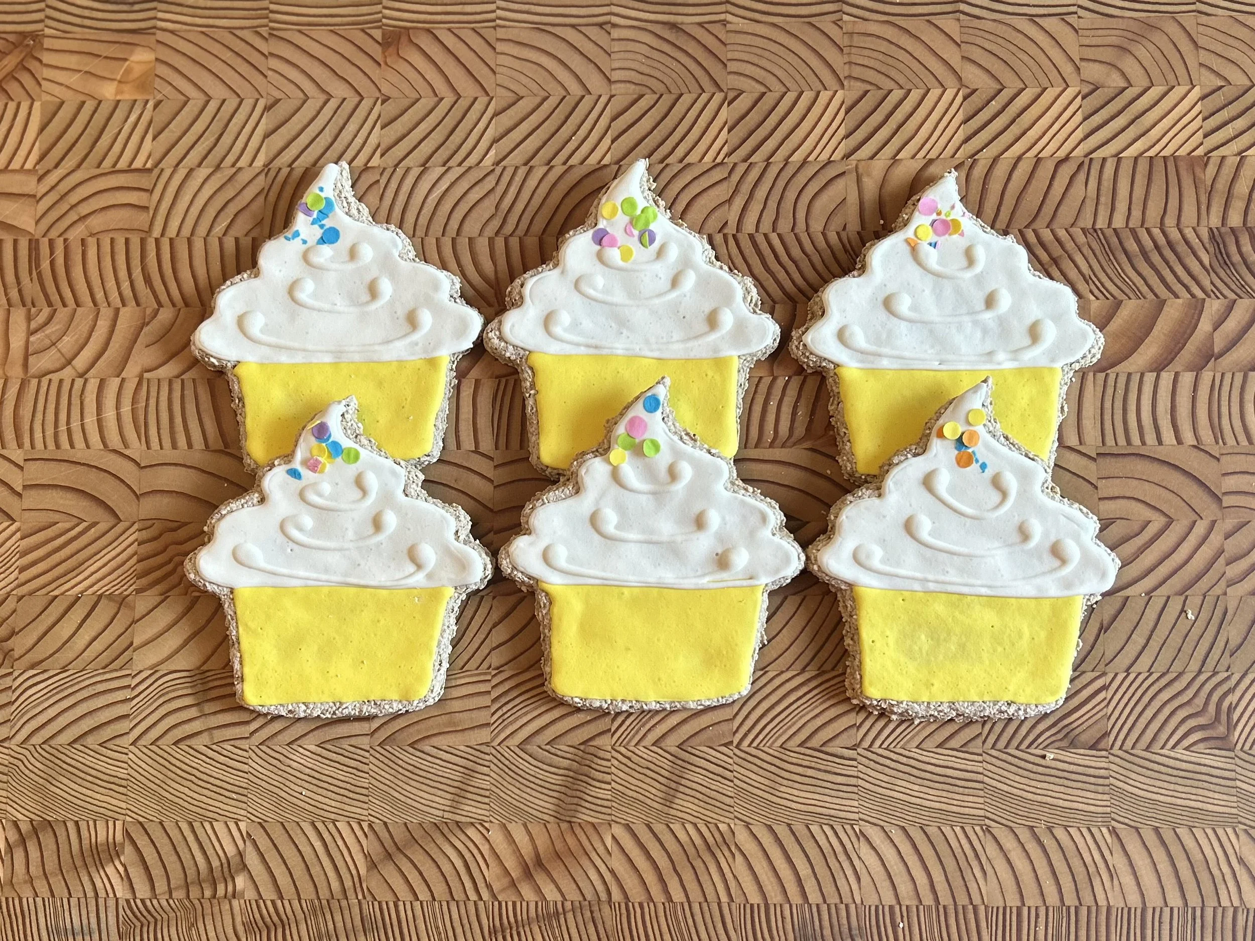 Dog cookies shaped like Birthday cup cakes with white icing and yellow base by Day of the Dob Bakery