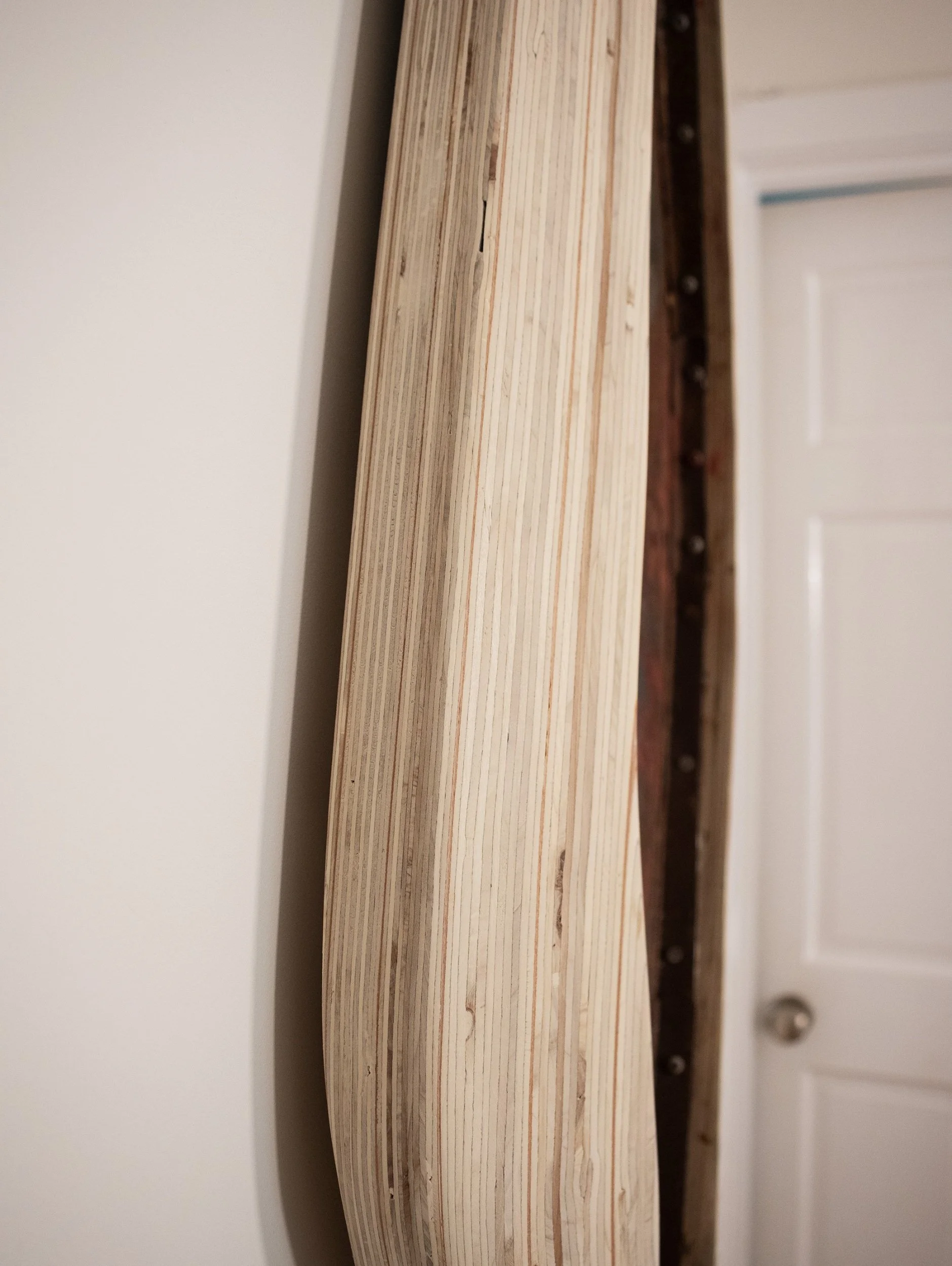 Close-up of a wooden frame with visible nails and inner wood layers, standing against a white wall.
