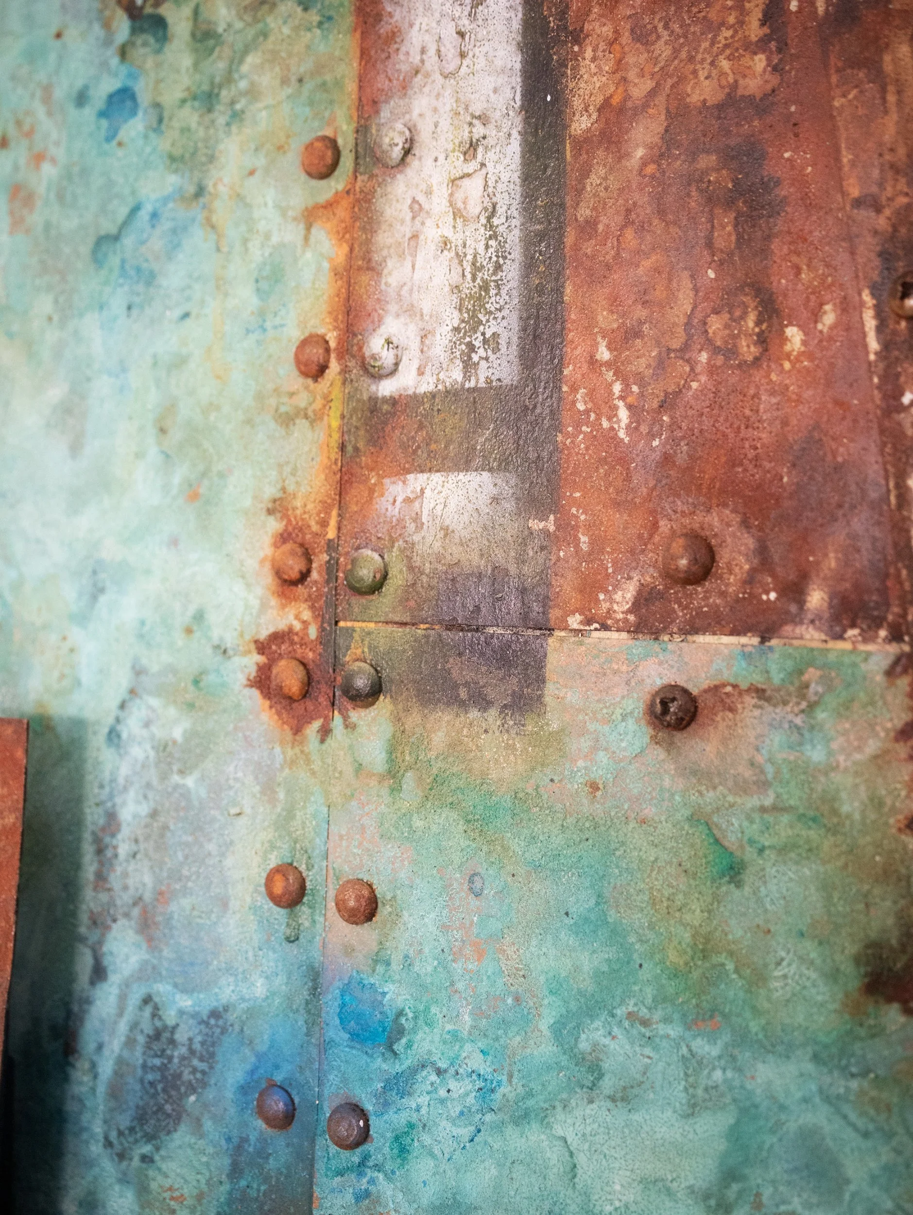 Close-up of a rusty metal surface with multiple rusted bolts and peeling green, red, and blue paint.