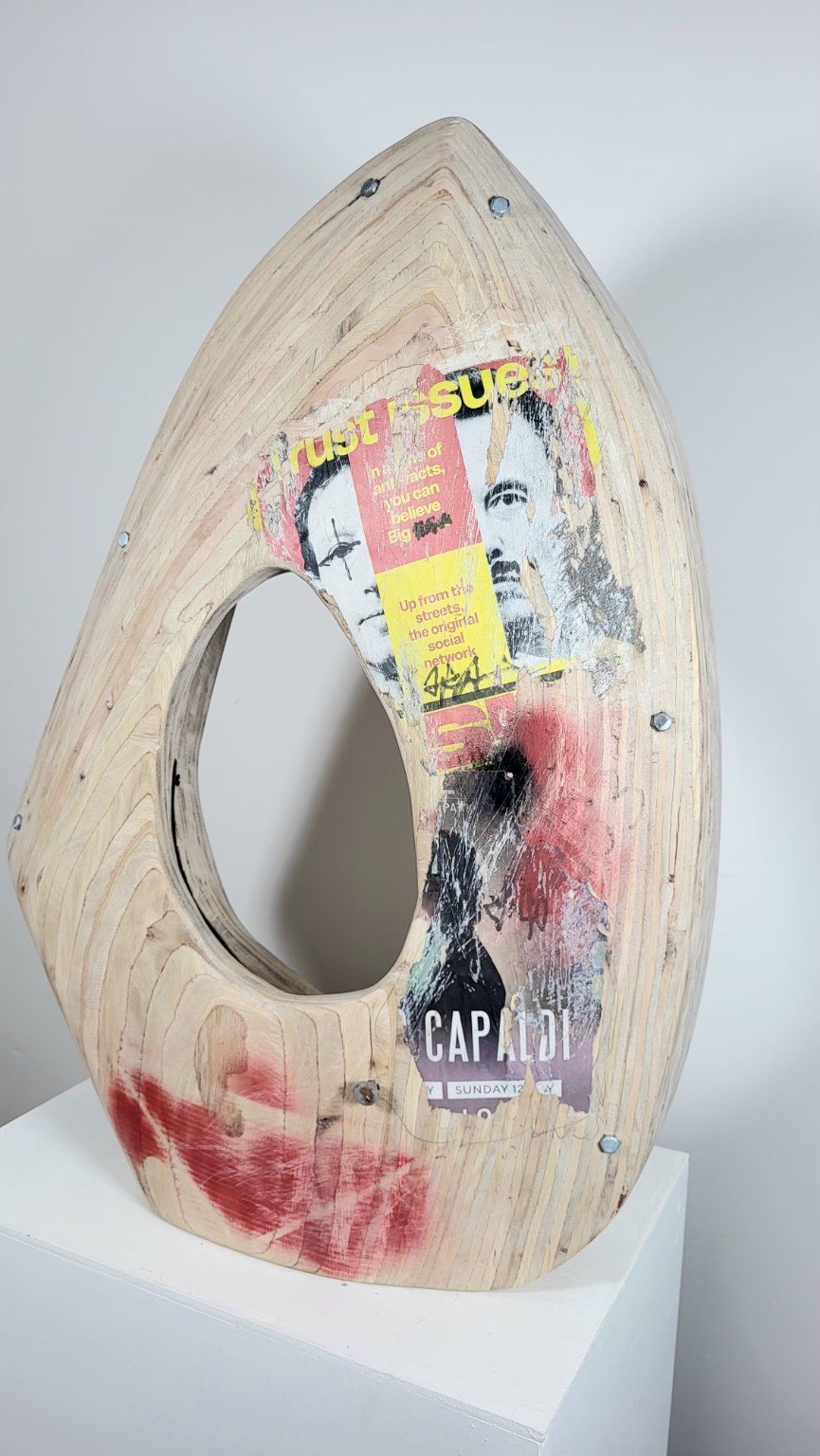 A wooden sculptural artwork with torn posters and graffiti spray paint.
