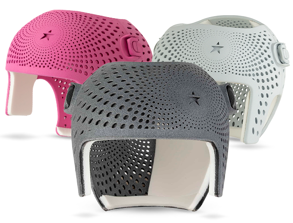 Three protective helmets in pink, gray, and white with ventilation holes and adjustable straps.