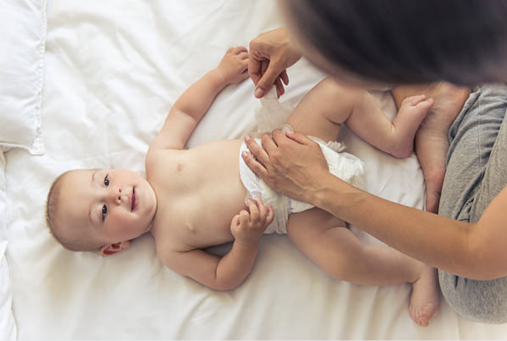 A young toddler lying on a bed, smiling, while an adult, possibly a parent, is dressing or changing the child's diaper.