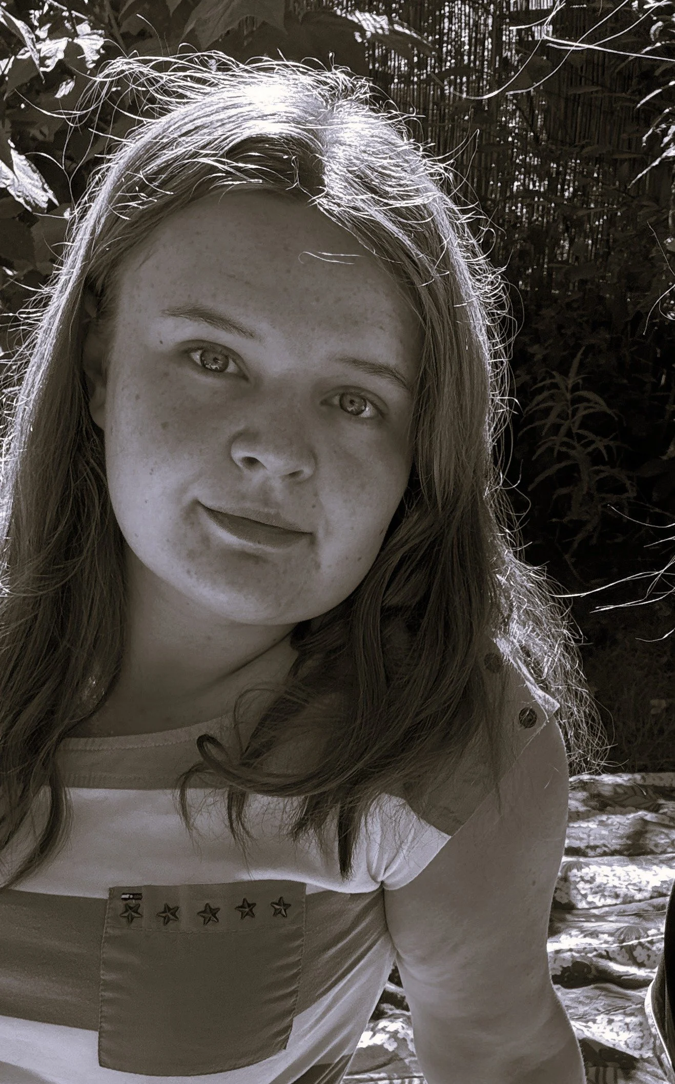 En ung kvinna med ljus hår och ljus hud, tagen utomhus med blad och buskar i bakgrunden, i svartvitt.