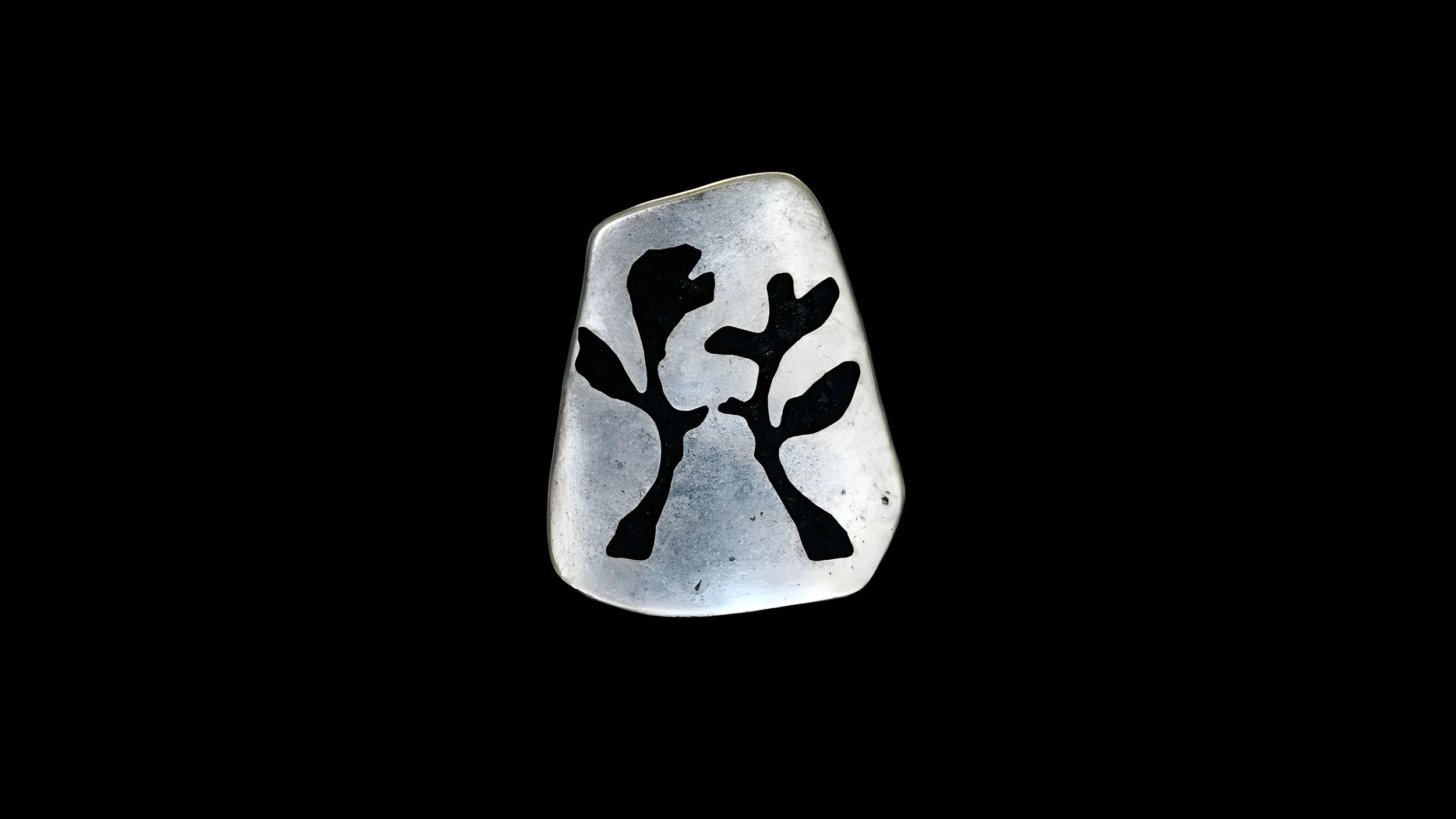 Silver ring with a black tree design on top, isolated on black background.