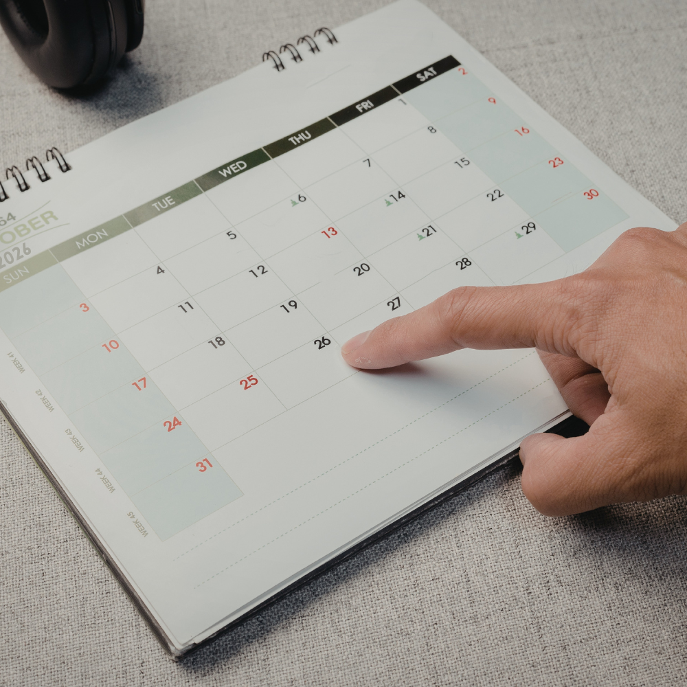 A person's hand pointing at October 27 on a desk calendar showing October 2026.