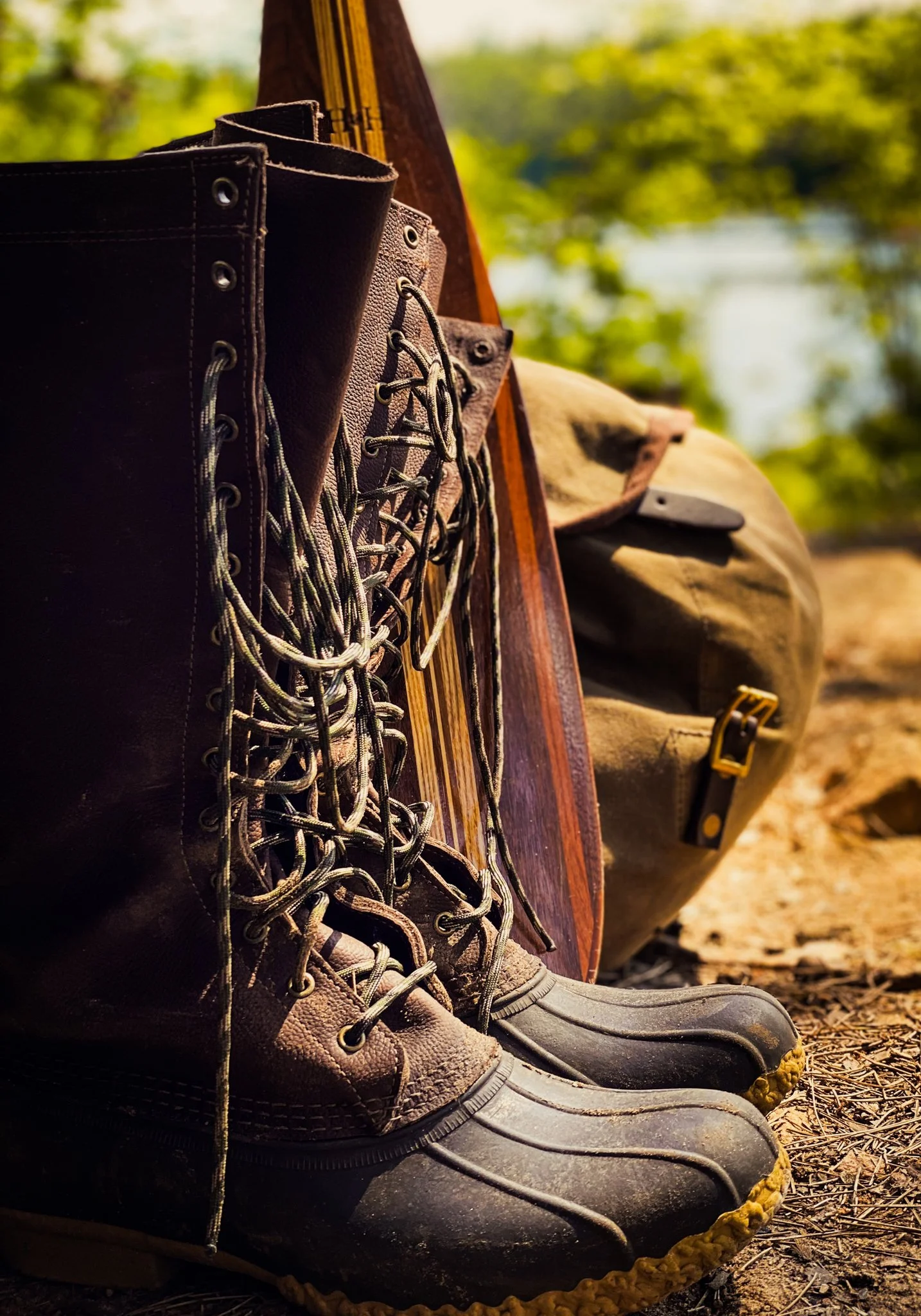 Hiking boots and gear outdoors near a lake with trees in the background.