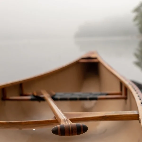 Close-up of a wooden canoe on a foggy lake, with trees in the distant background.