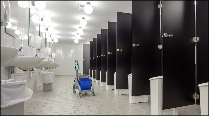 Public bathroom with multiple stalls, sinks, and mirrors, with a cleaning cart in the aisle.