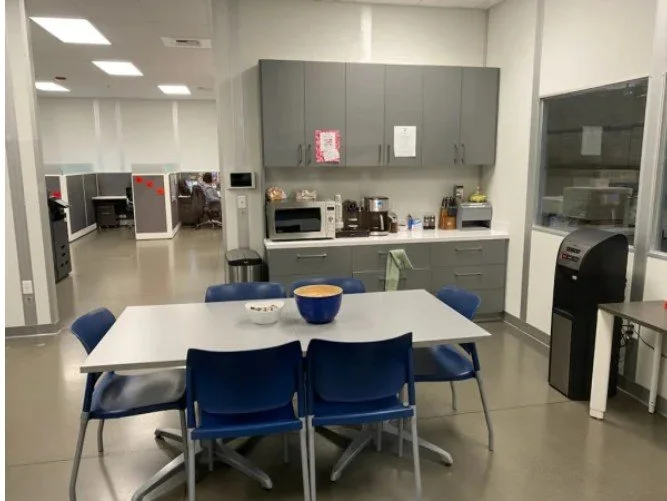 Office kitchenette with table, chairs, microwave, coffee machine, and water dispenser.