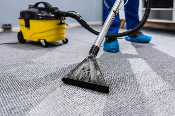 A person using a carpet cleaning machine with a yellow and black vacuum unit to clean a gray carpet.