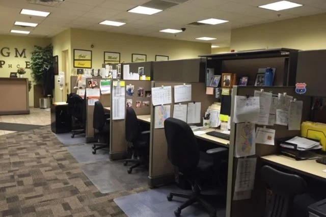 Office cubicles with computers, office chairs, and various papers and personal items in a professional environment.