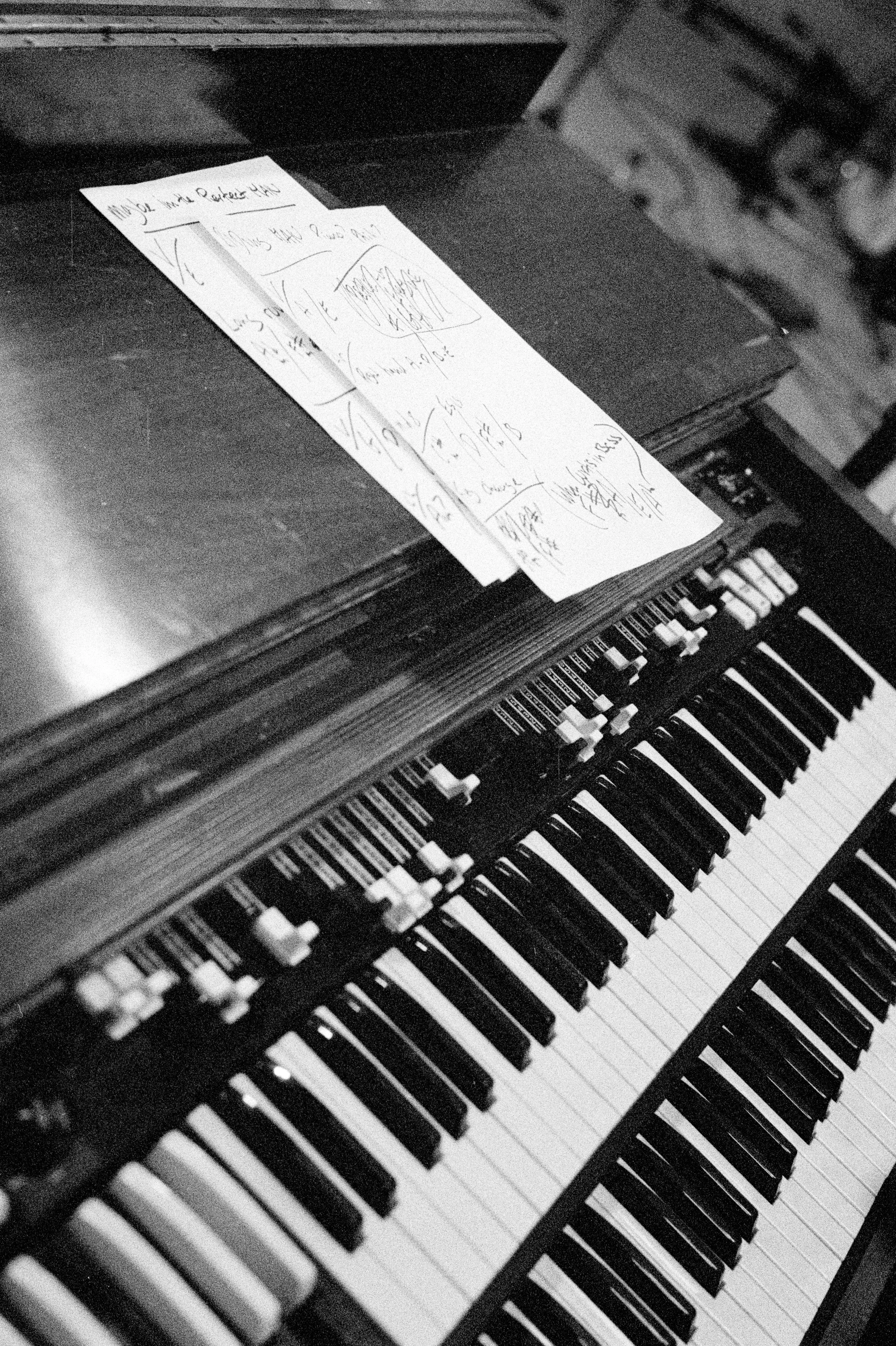 A black and white photo of a piano keyboard with handwritten sheet music on top of it.
