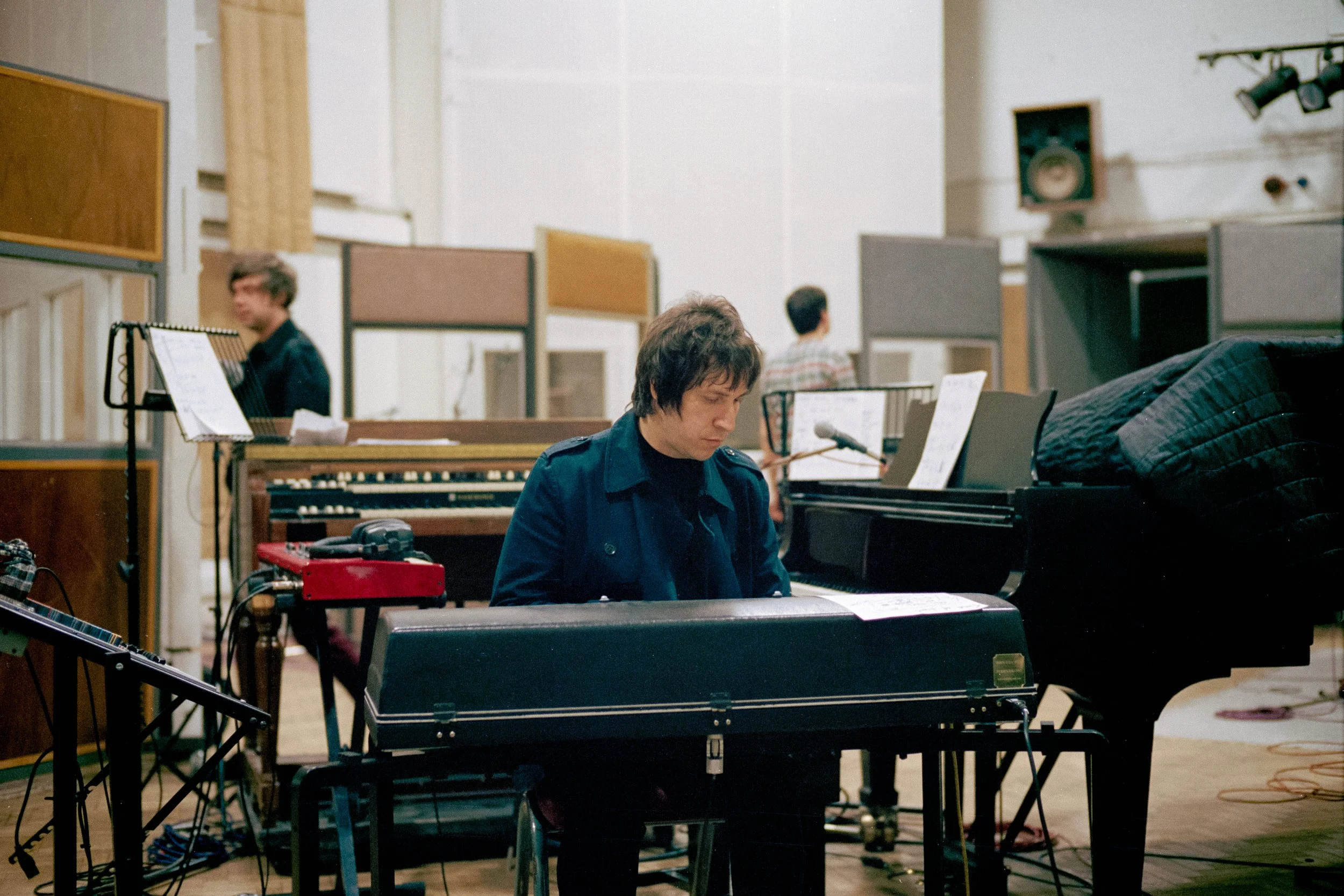 A person playing a keyboard in a recording studio with other musicians and equipment around.