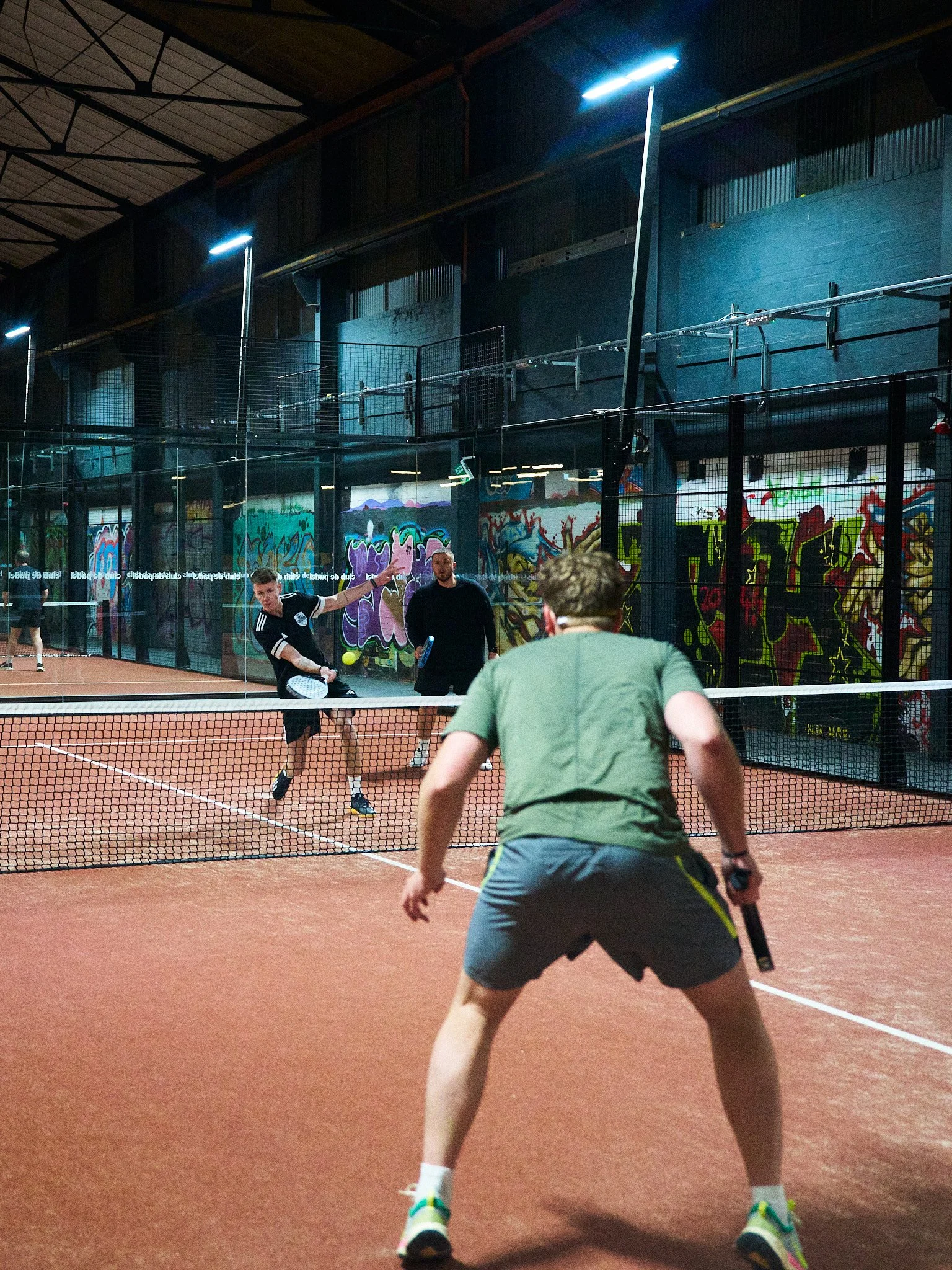 People playing pickleball on an indoor court with graffiti walls in the background.