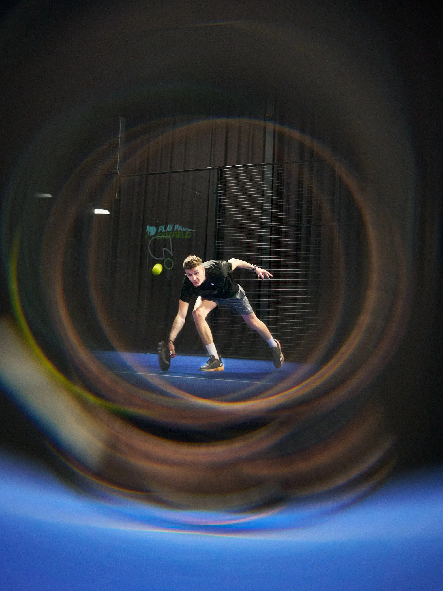 A young man playing padel on an indoor court, reaching for the ball, abstract