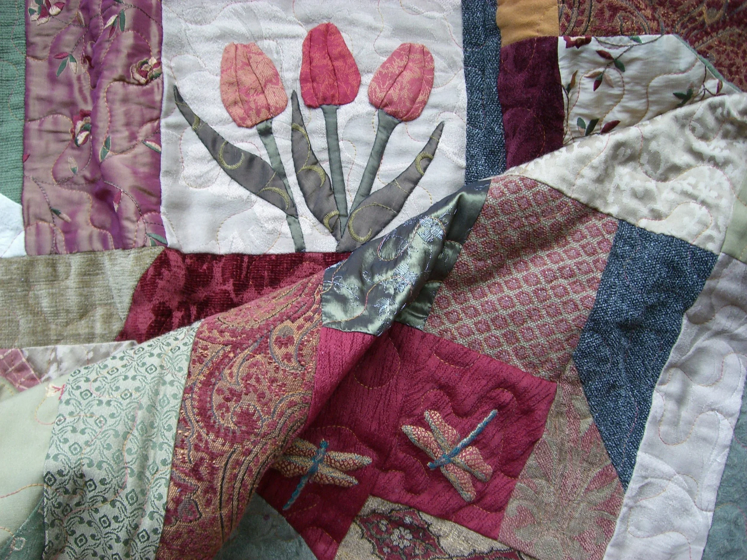 A close-up of a colorful quilt with floral, dragonfly, and geometric patterns.