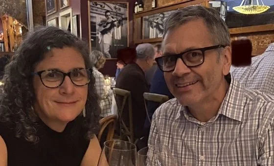 Kathryn Rodenmeyer and Ron Rodenmeyer sitting at a restaurant table, smiling at the camera, with other patrons in the background.