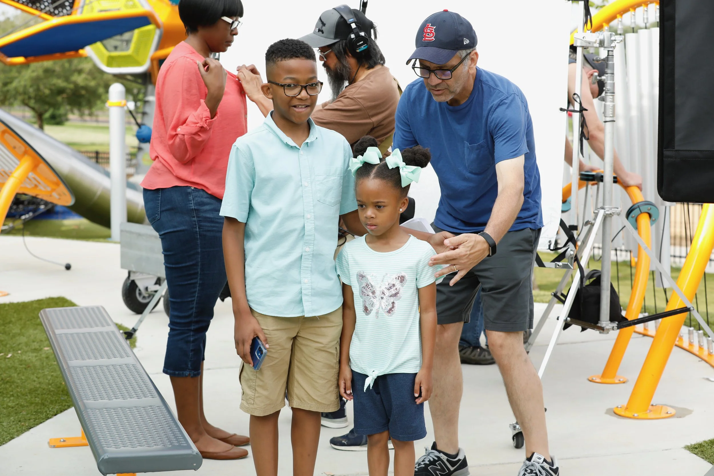 Children getting their photos taken at an outdoor science exhibit. An adult shows something to a young girl with puffy hair and bows, while a boy and older girl wait nearby.
