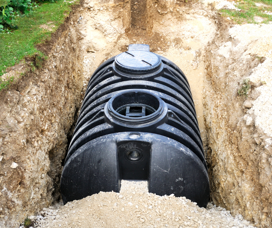 Installing a large black septic tank in a trench with exposed soil on either side.