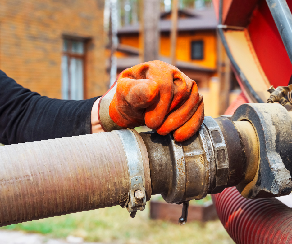 A person wearing a black long-sleeve shirt and orange work gloves tightening a large metal pipe with a wrench outdoors.