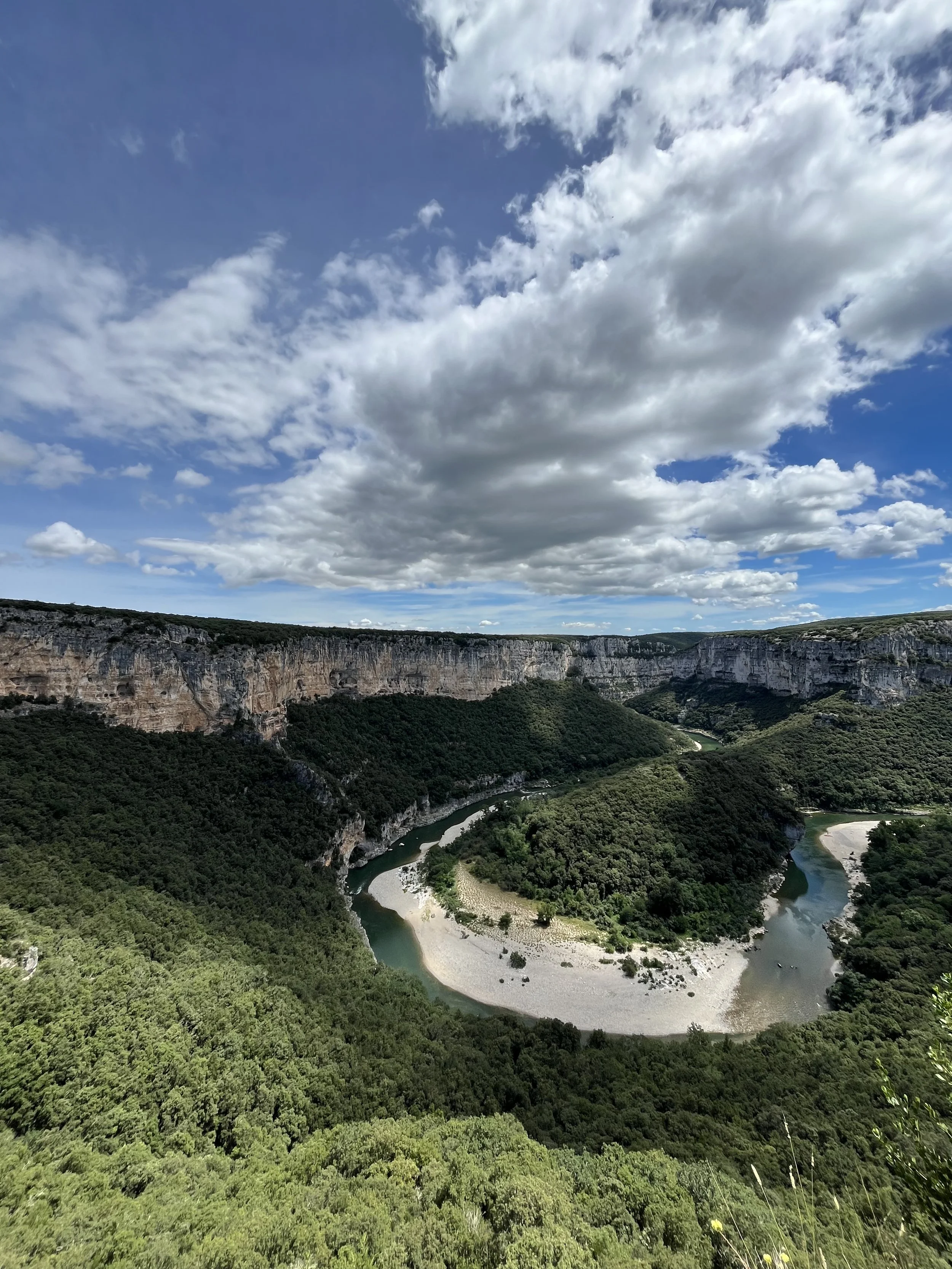 A winding river flowing through a lush green canyon with high cliffs and a partly cloudy sky overhead.