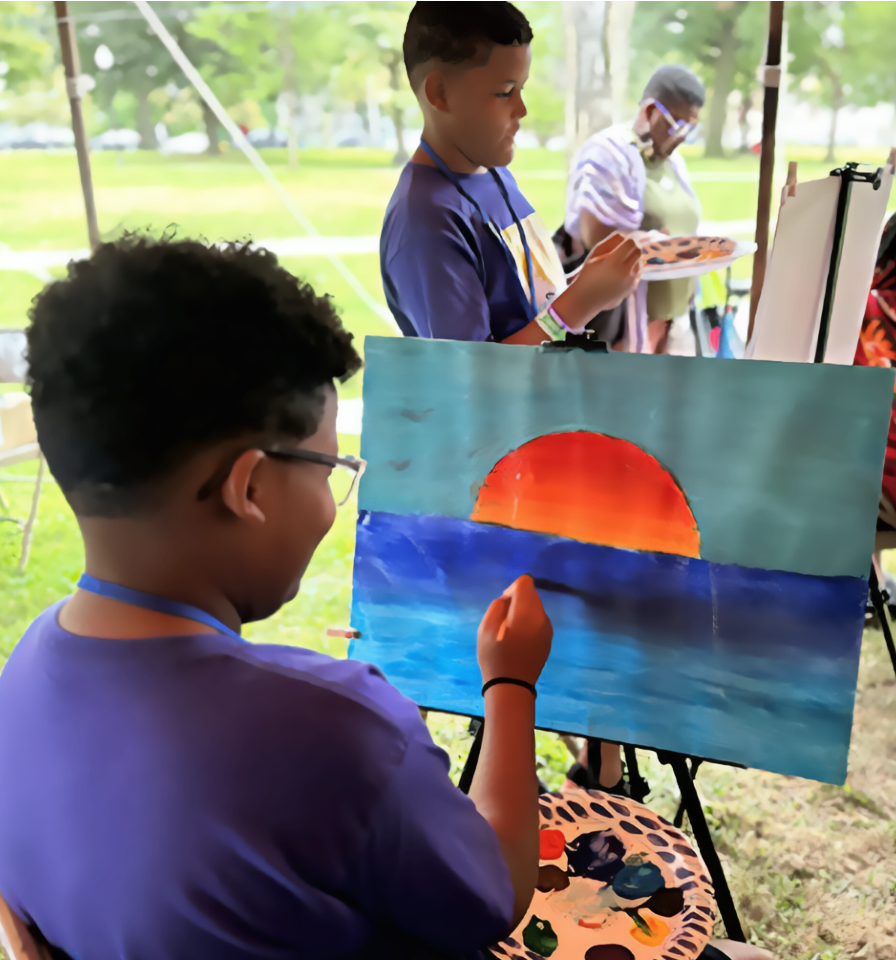 Children participating in a painting activity outdoors, with one child painting a sunset over water and others observing or painting at nearby easels.