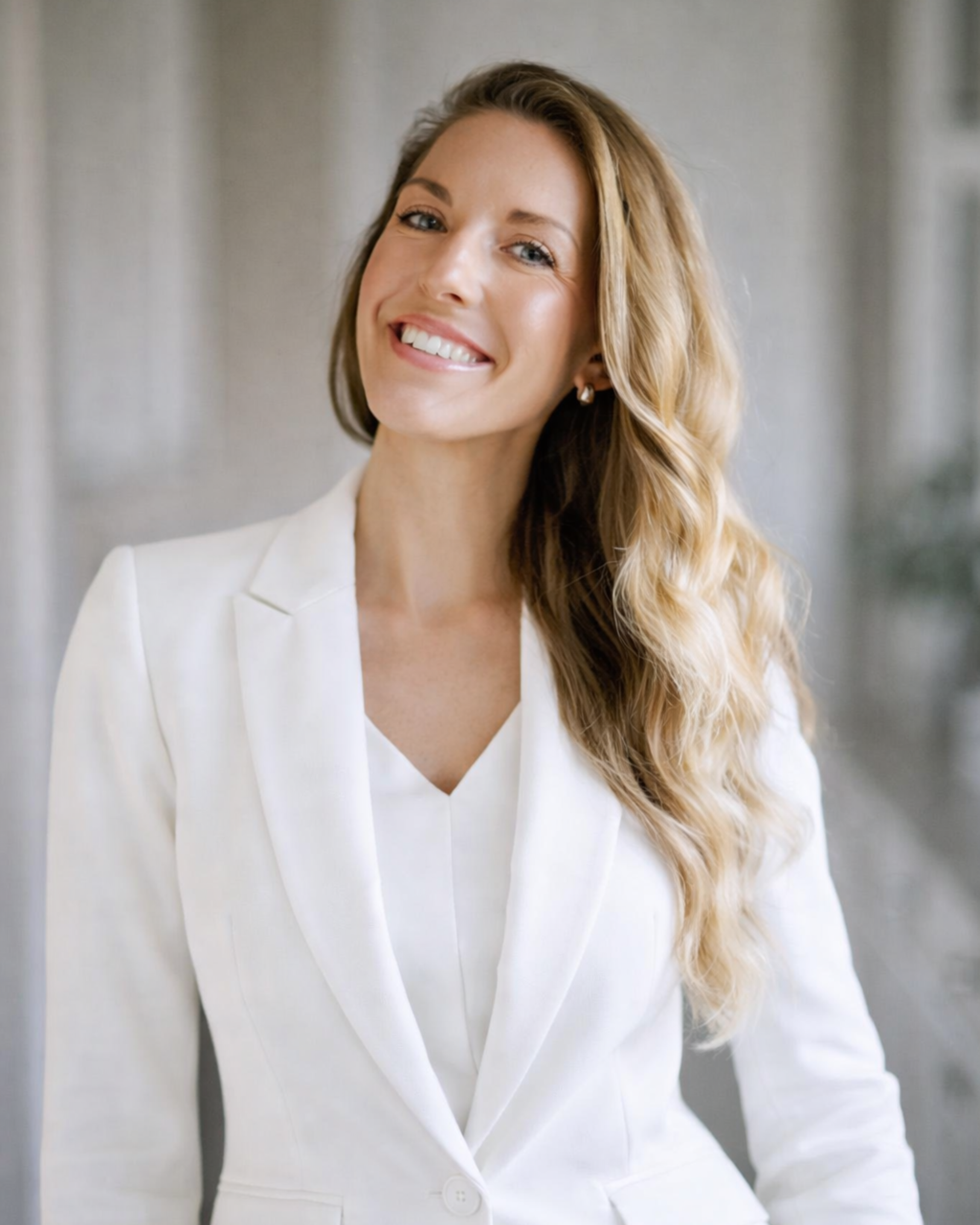 A woman with long, wavy blonde hair smiling in a white blazer and blouse.