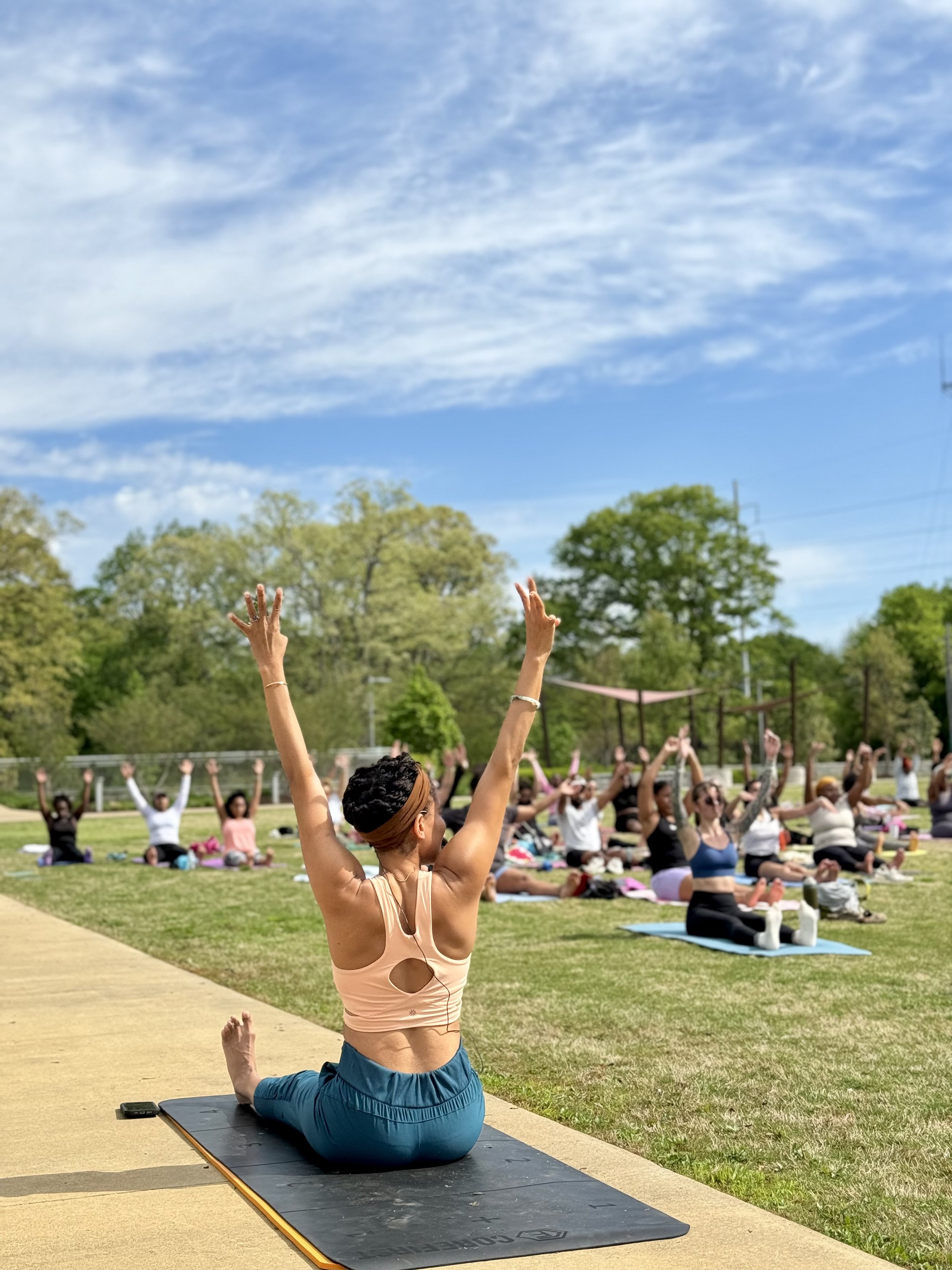 Khetanya teaching a Pilates in the Park class on the green space in Grant Park, Atlanta, surrounded by trees, blue skies, and community members.