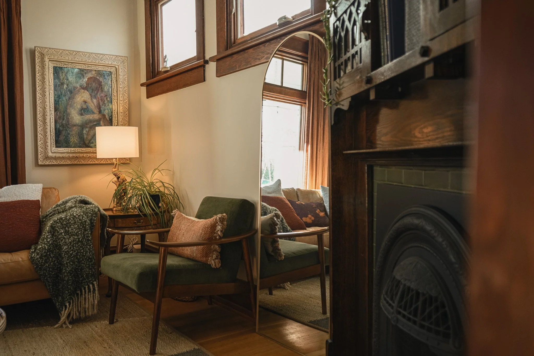 Curated Style Collective-designed living room with vintage woodwork, olive green lounge chair, arched floor mirror, layered textiles, original fireplace and warm natural light.