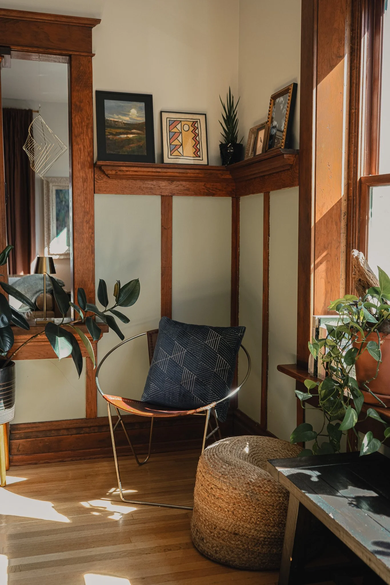 Curated Style Collective-designed corner featuring original Craftsman woodwork, vintage metal and leather chair, graphic pillow and layered indoor plants.