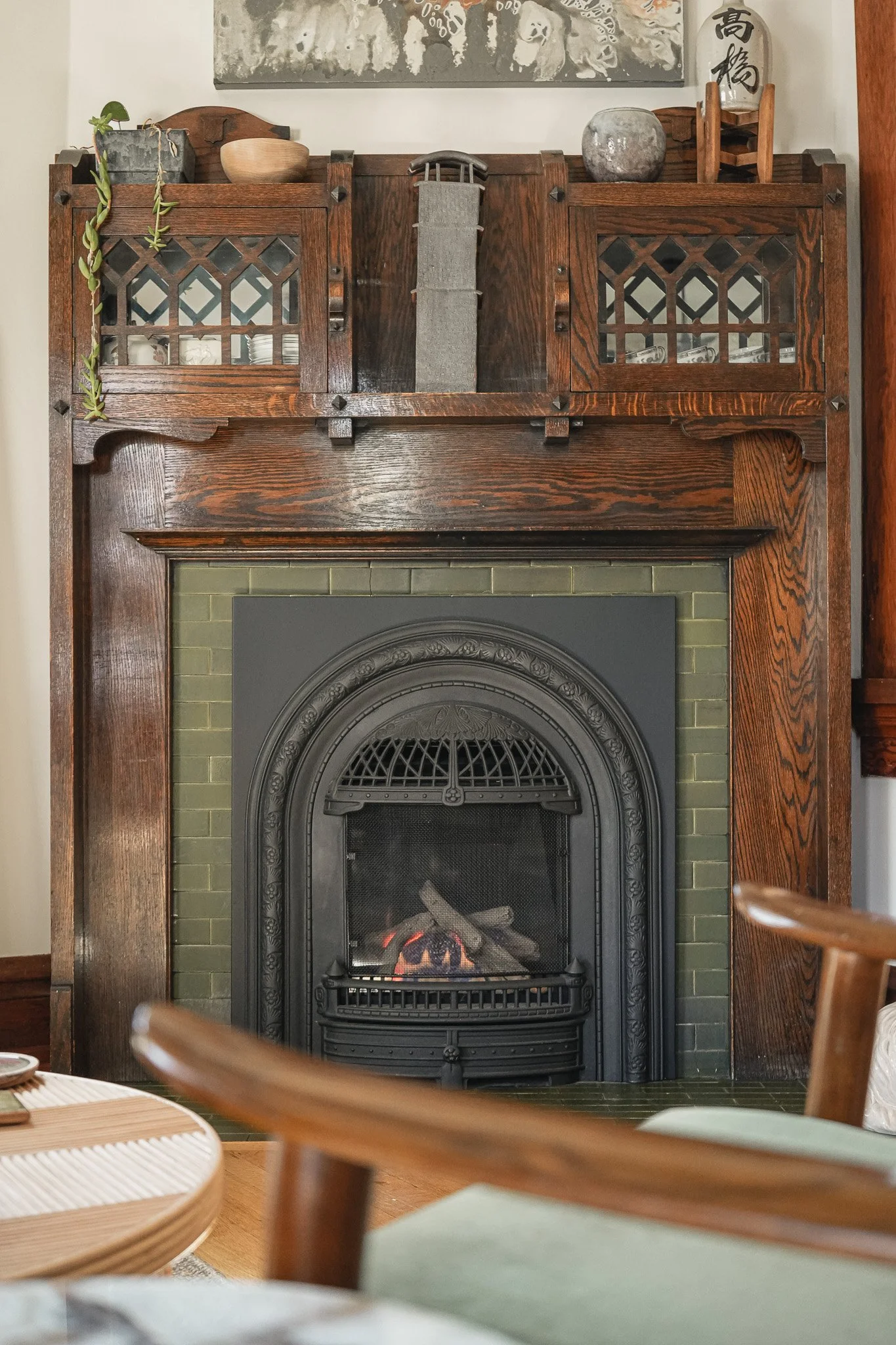 Original Craftsman fireplace styled by Curated Style Collective with green tile surround, carved dark wood mantel and decorative cast-iron firebox.