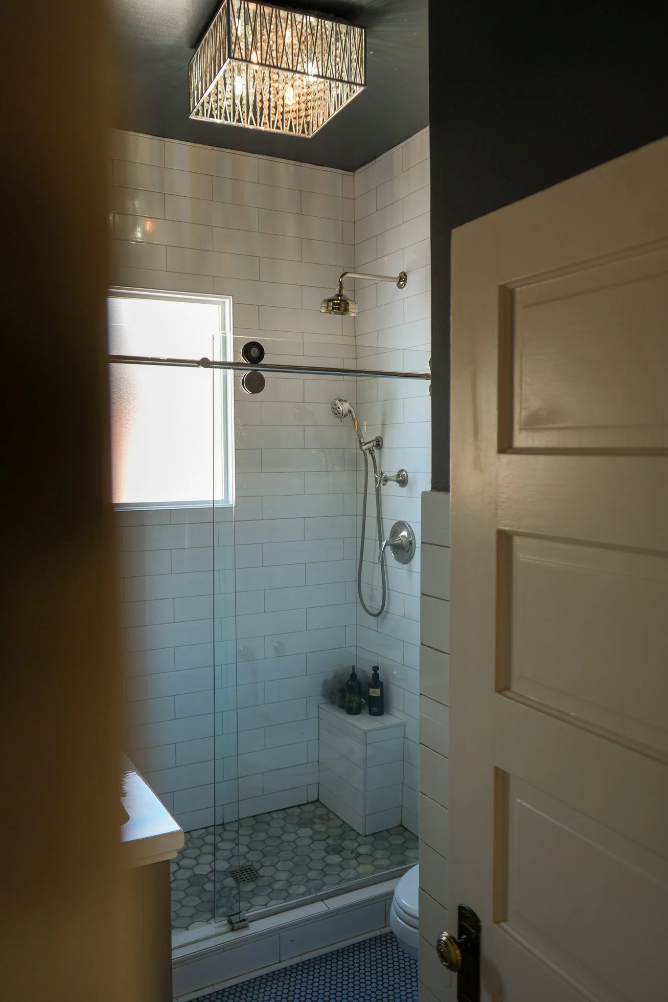 Curated Style Collective-designed bathroom with white subway tile shower, polished metal fixtures, frosted window and warm natural light.