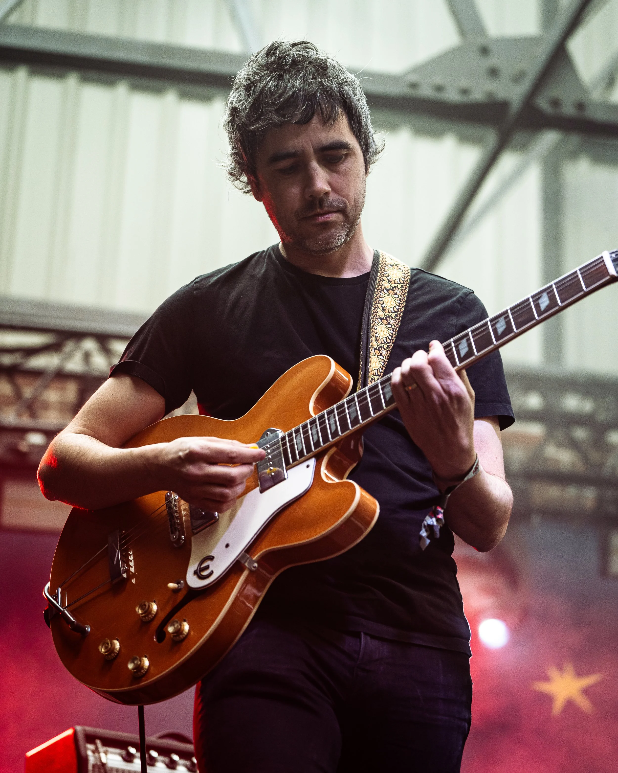 A man playing an electric guitar on stage with a blurred background that has a star and lighting effects.