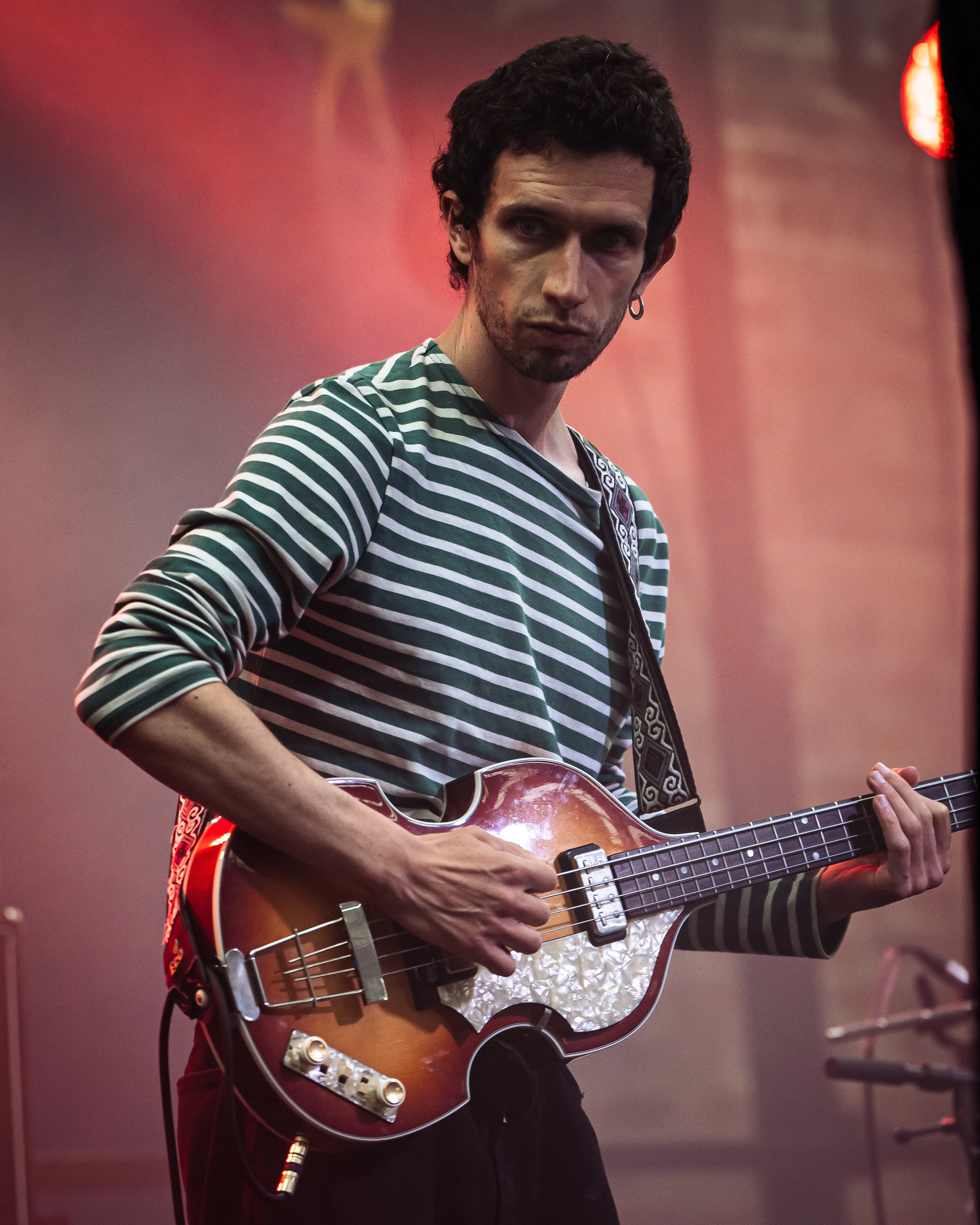 A person with dark curly hair, wearing a striped green and white shirt, playing an electric guitar with a sunburst finish during a performance.
