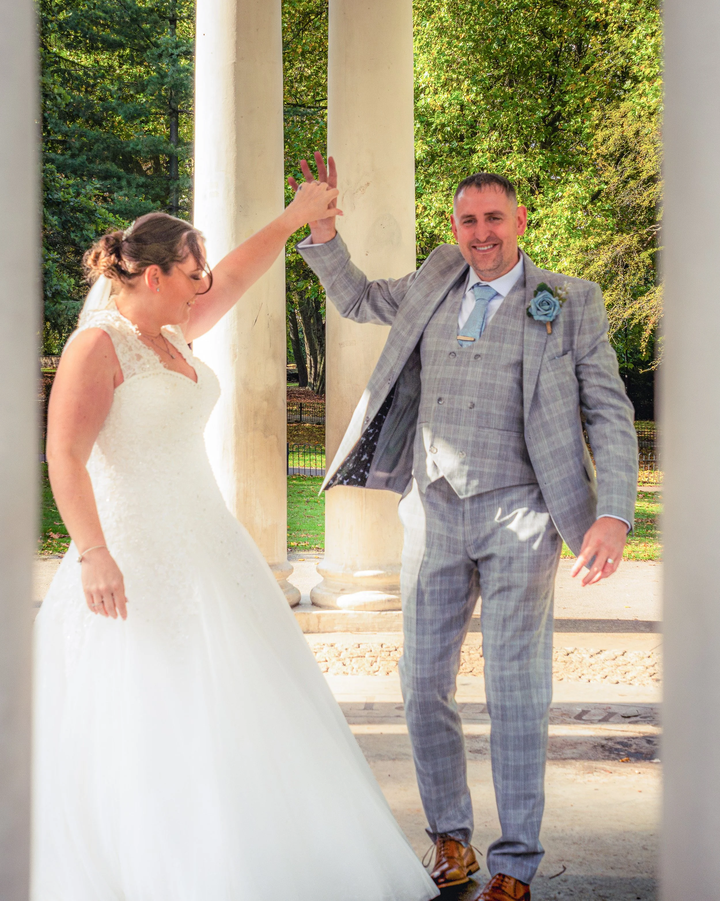 A newlywed couple dancing outdoors under a pavilion, with trees in the background.