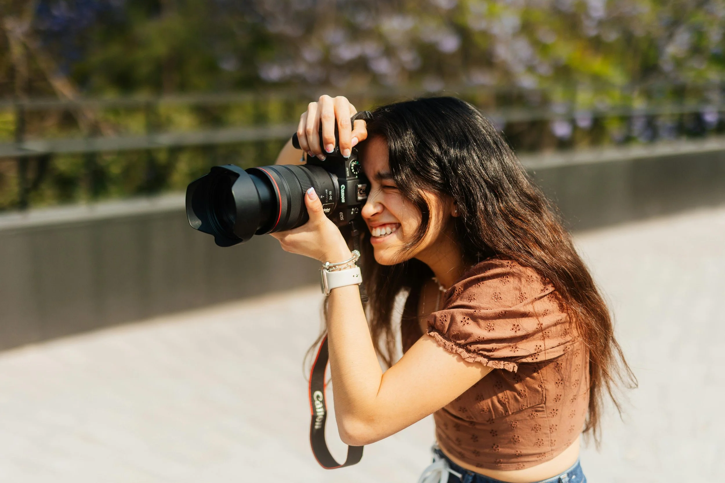 Woman smiling while taking a photograph with a professional camera outdoors.