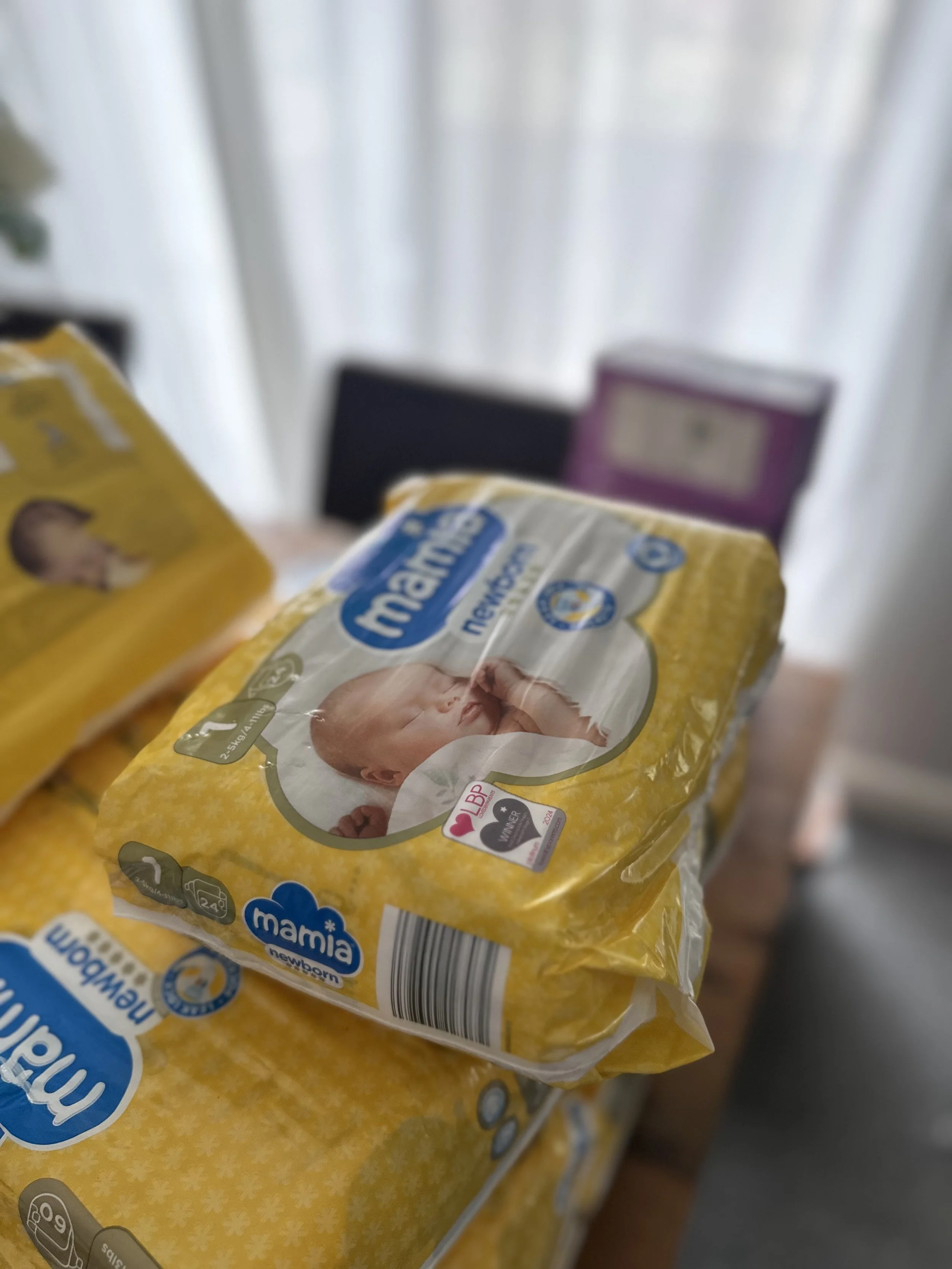 A pack of Mamilia newborn baby diapers on a table, with other similar diaper packs visible in the background.