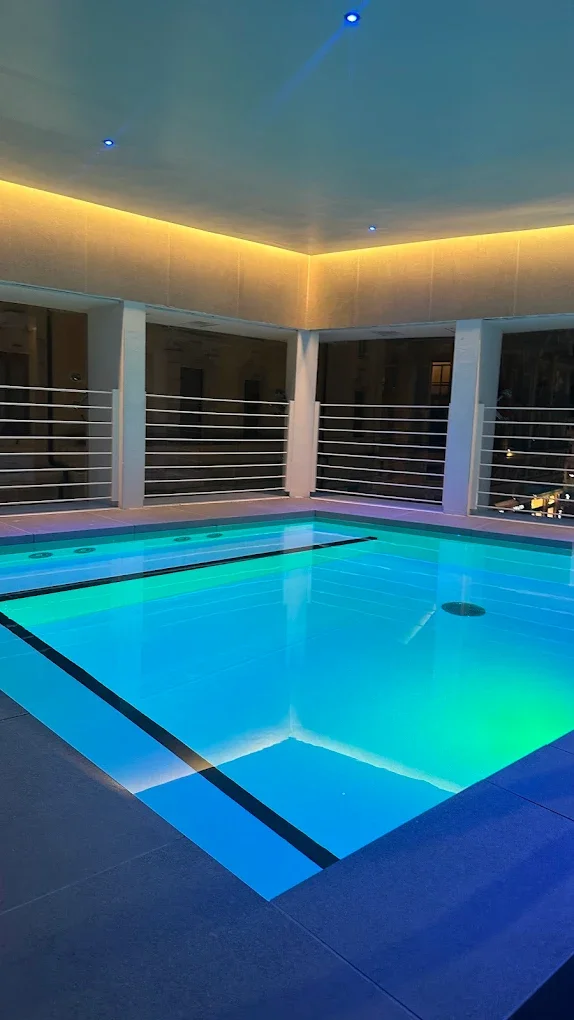 Indoor rooftop pool with colored lighting and high glass barriers, illuminated ceiling with small blue lights.