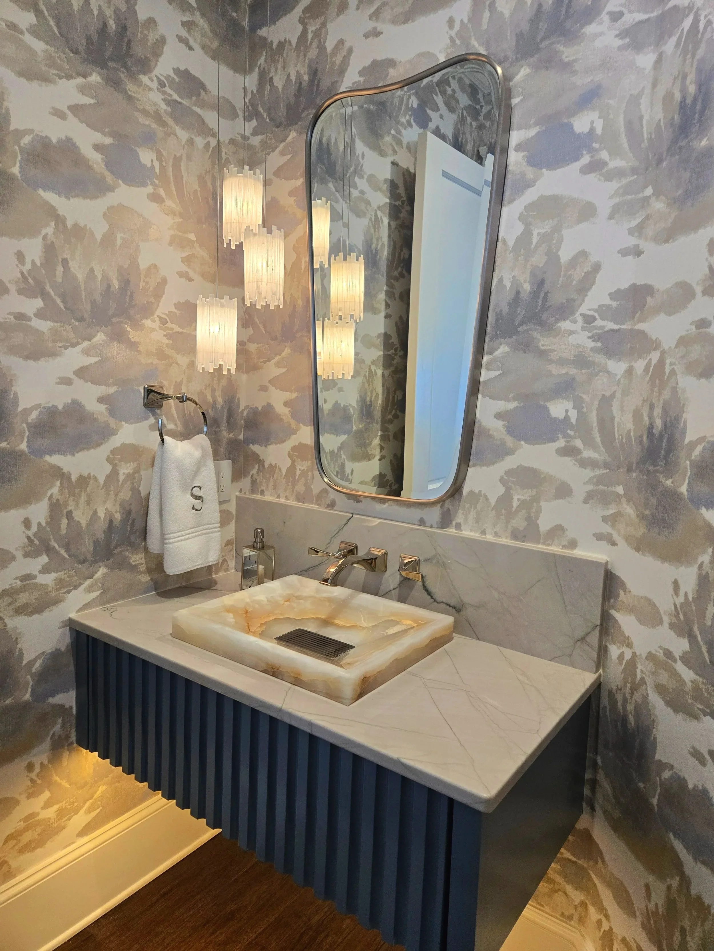 Modern bathroom with floral patterned wallpaper, a marble countertop with a vessel sink, a wall-mounted mirror, and hanging light fixtures.