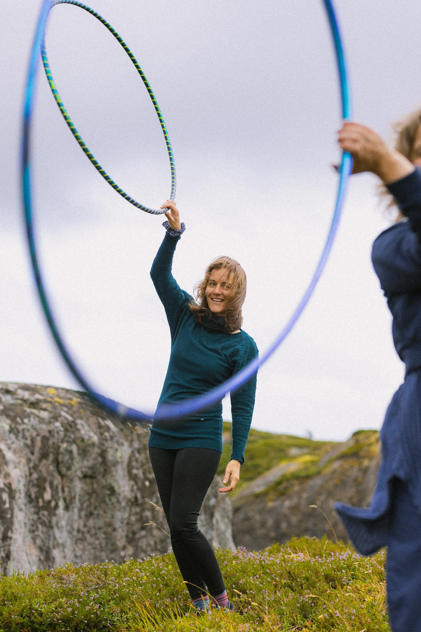 Two women outdoors playing with hula hoops, with one woman smiling and lifting a hoop.