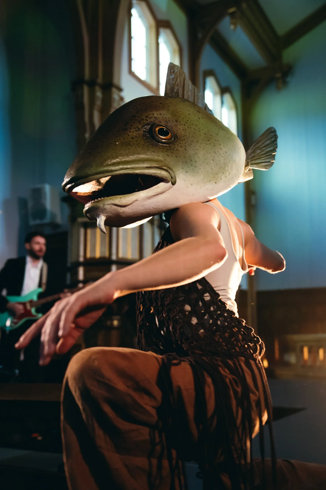 Person with a fish mask performing on stage with a guitarist in the background.