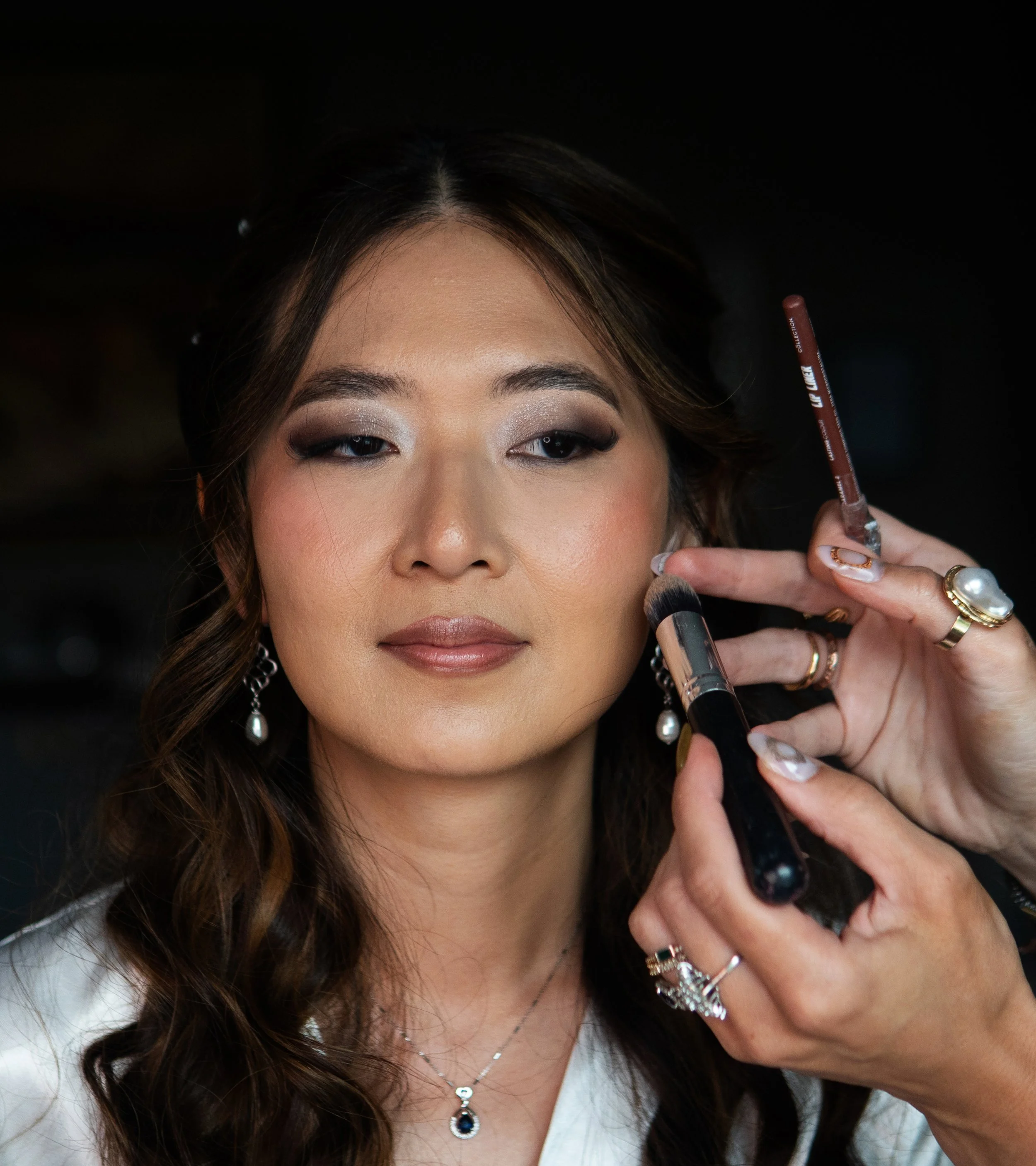 A woman having her makeup applied, focusing on her face with makeup brushes near her cheek.
